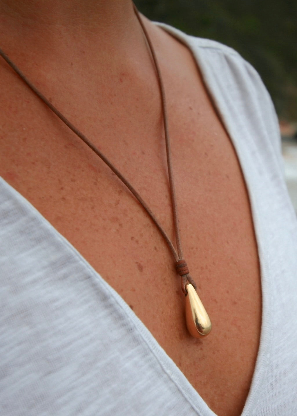 18K gold drop pendant necklace on leather cord worn on neck, St Barth beach