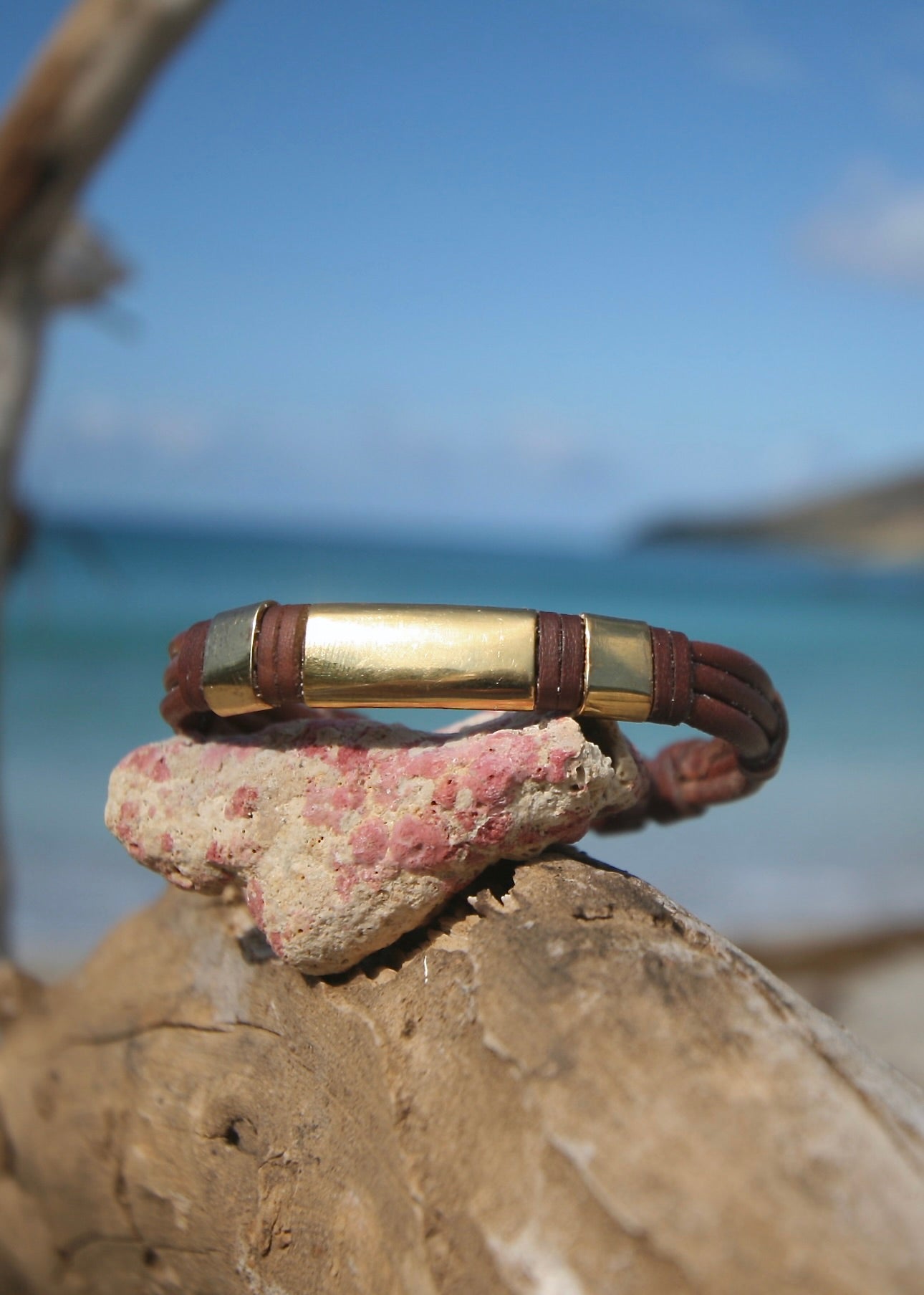 Trésors de St Barth 18K gold bars bracelet showing sculpted curve and sailor knots with Caribbean ocean behind resting on coral rock