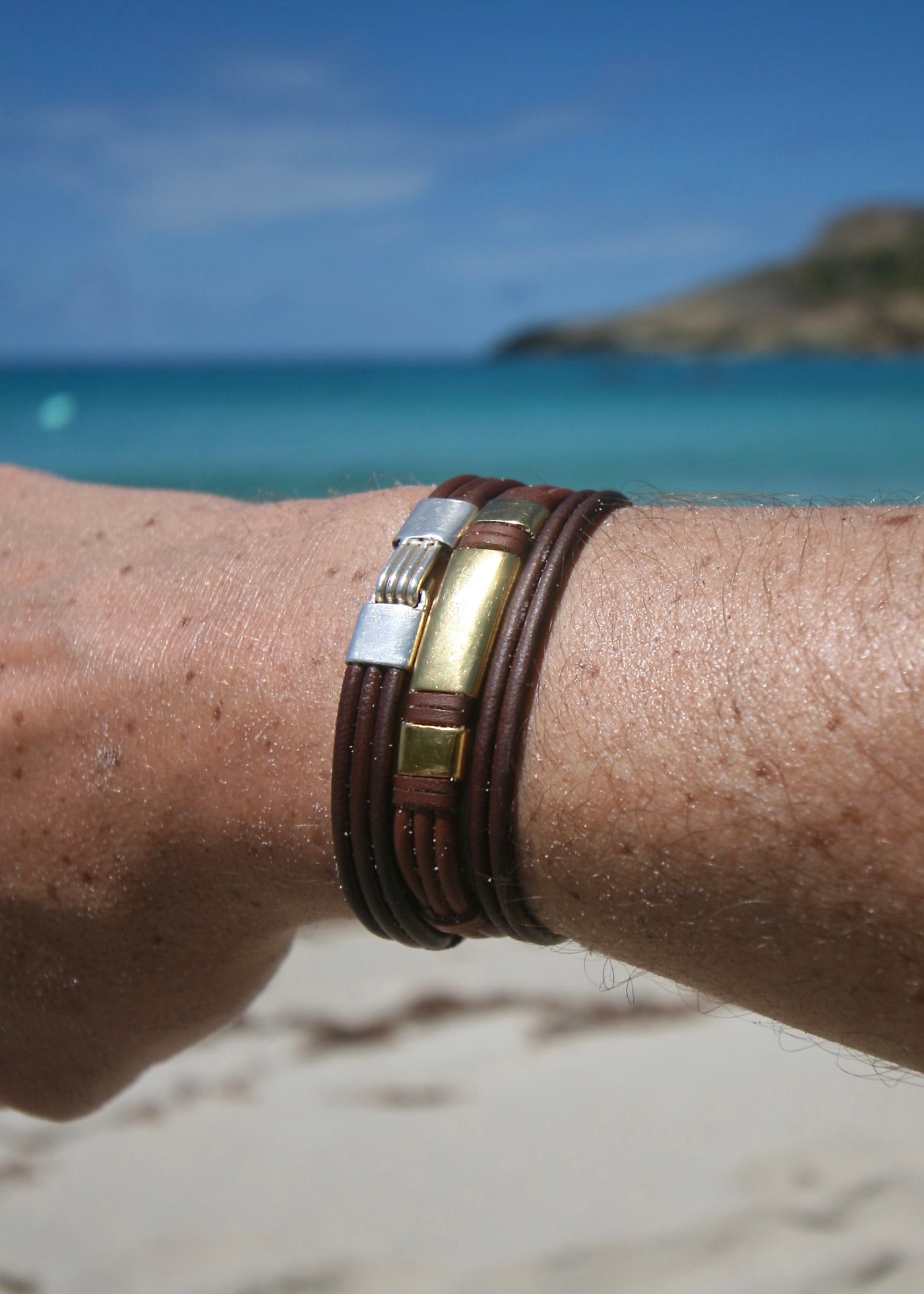 Triple 18K solid gold bar bracelet on kangaroo leather worn on wrist with St Barth beach in background