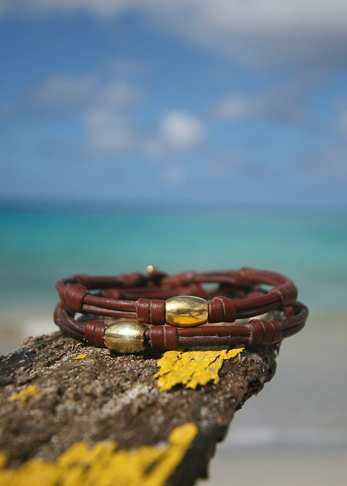 Handmade 18K gold bead bracelet on kangaroo leather with pearl clasp displayed on fishing net at beach