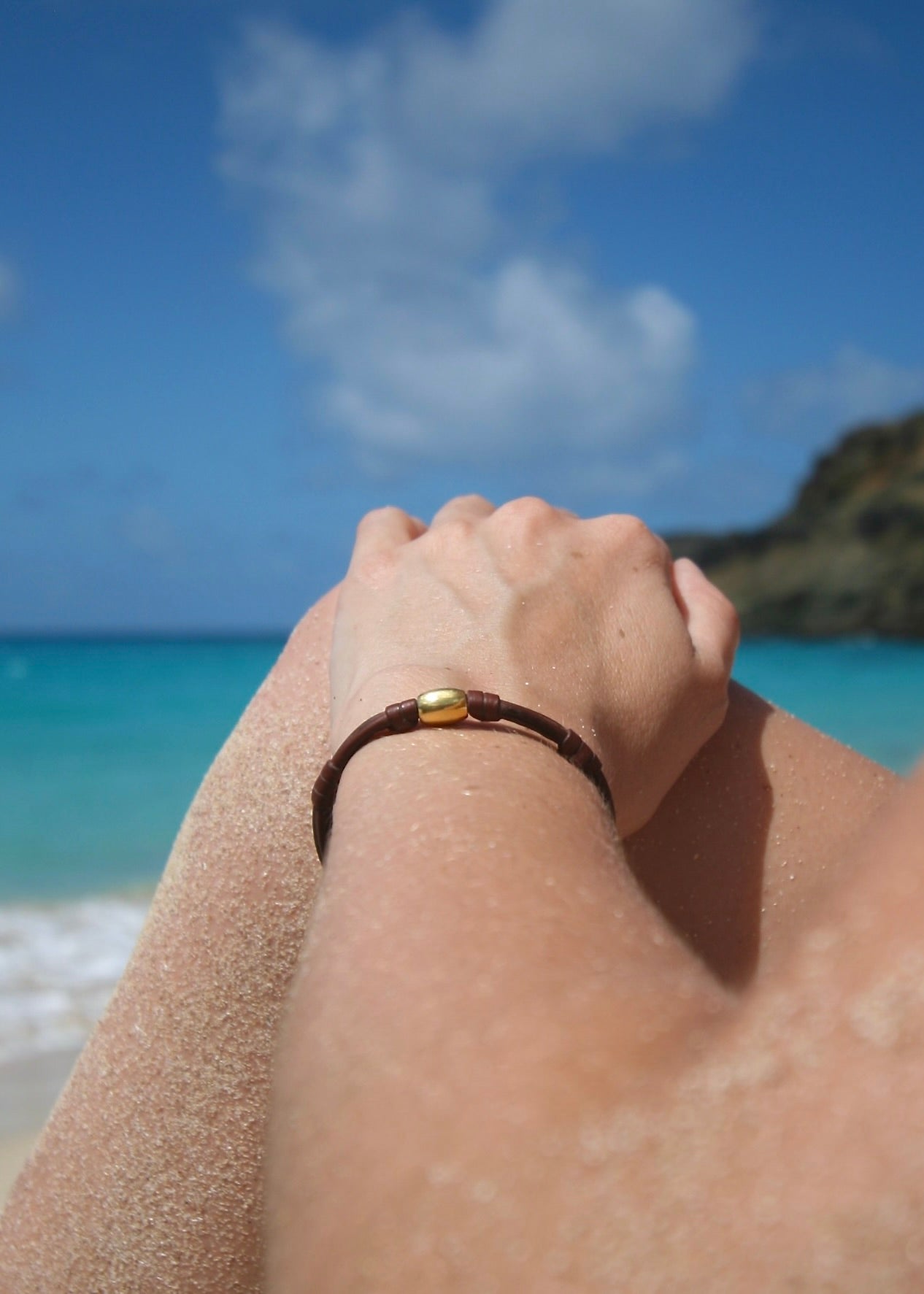 18K solid gold bead bracelet on kangaroo leather worn on wrist at the beach with sand and ocean behind