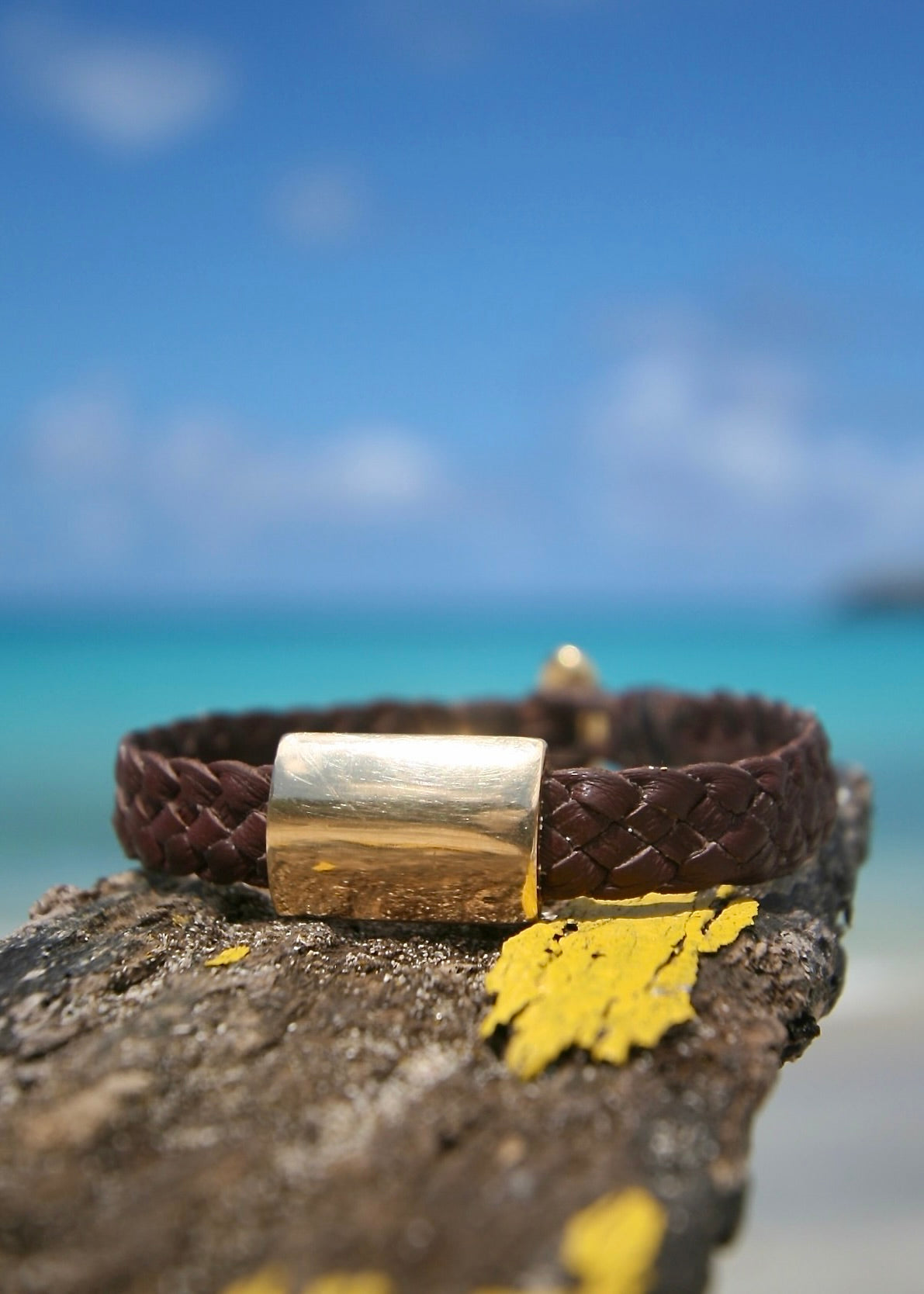 Close up of 18K solid gold sculpted element on hand braided kangaroo leather bracelet resting on stone