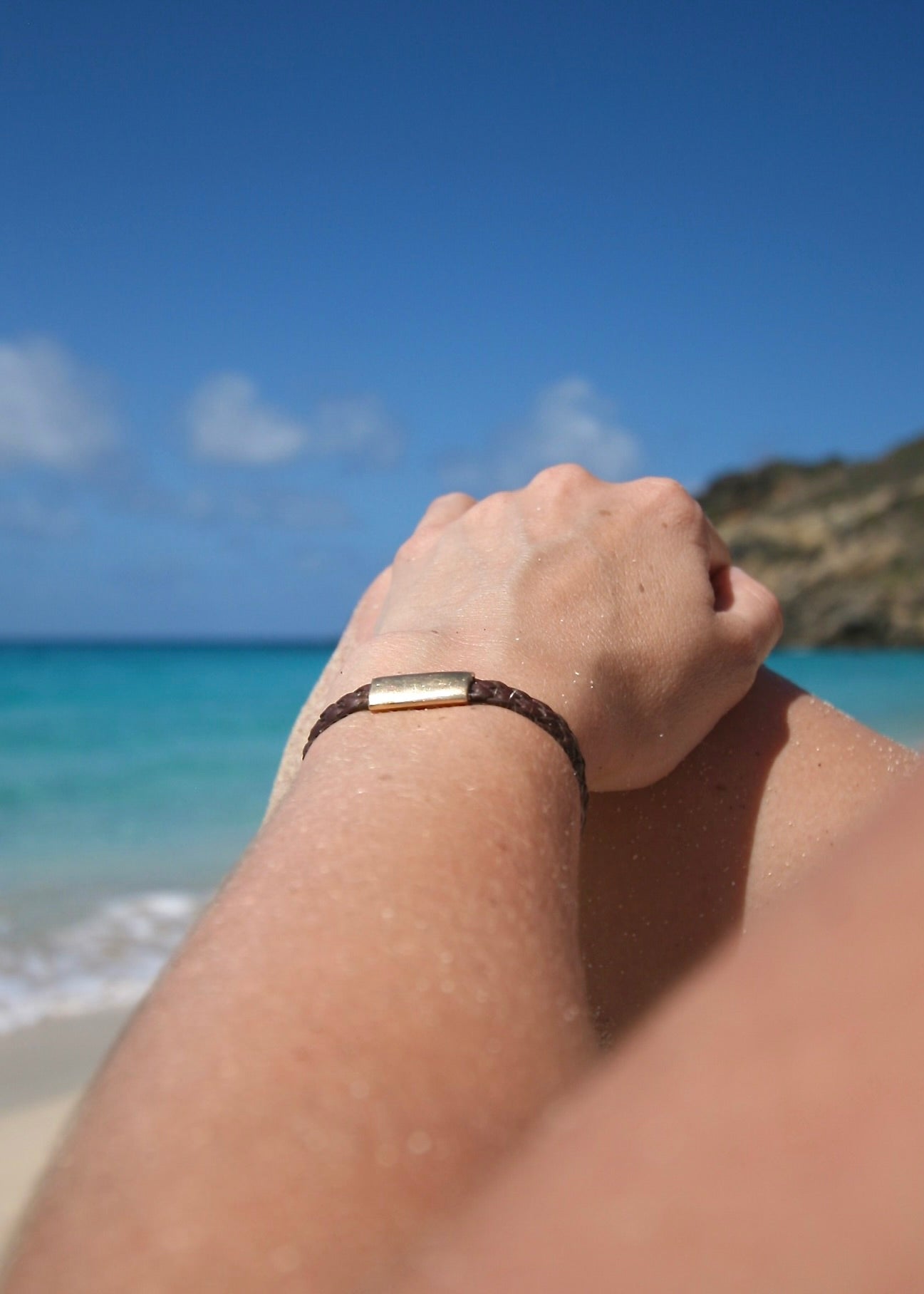 Trésors de St Barth 18K solid gold bracelet on braided kangaroo leather worn on wrist with ocean behind