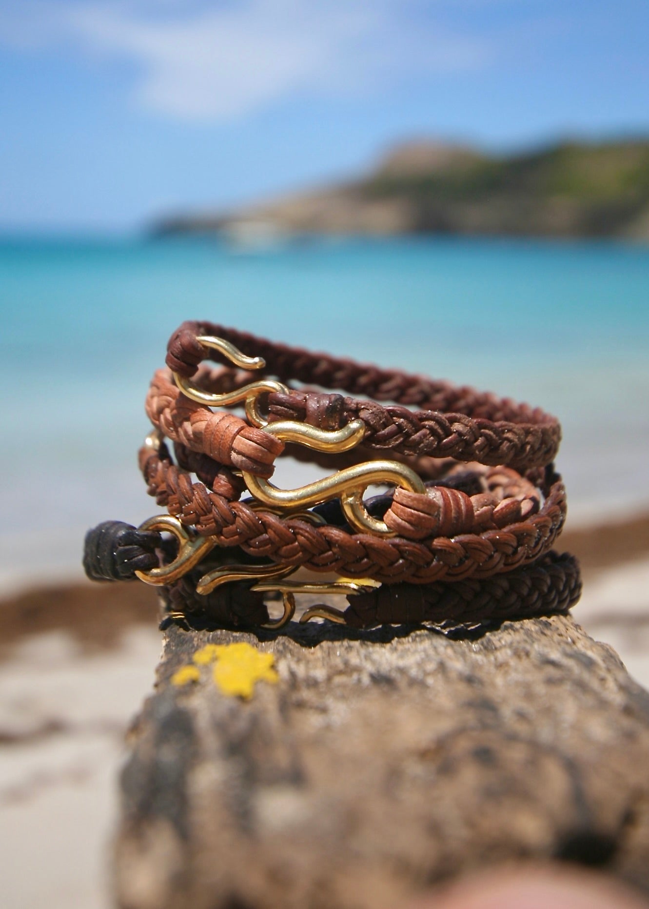 Handmade 18K gold fish hook bracelets on braided kangaroo leather hanging from wooden post at beach