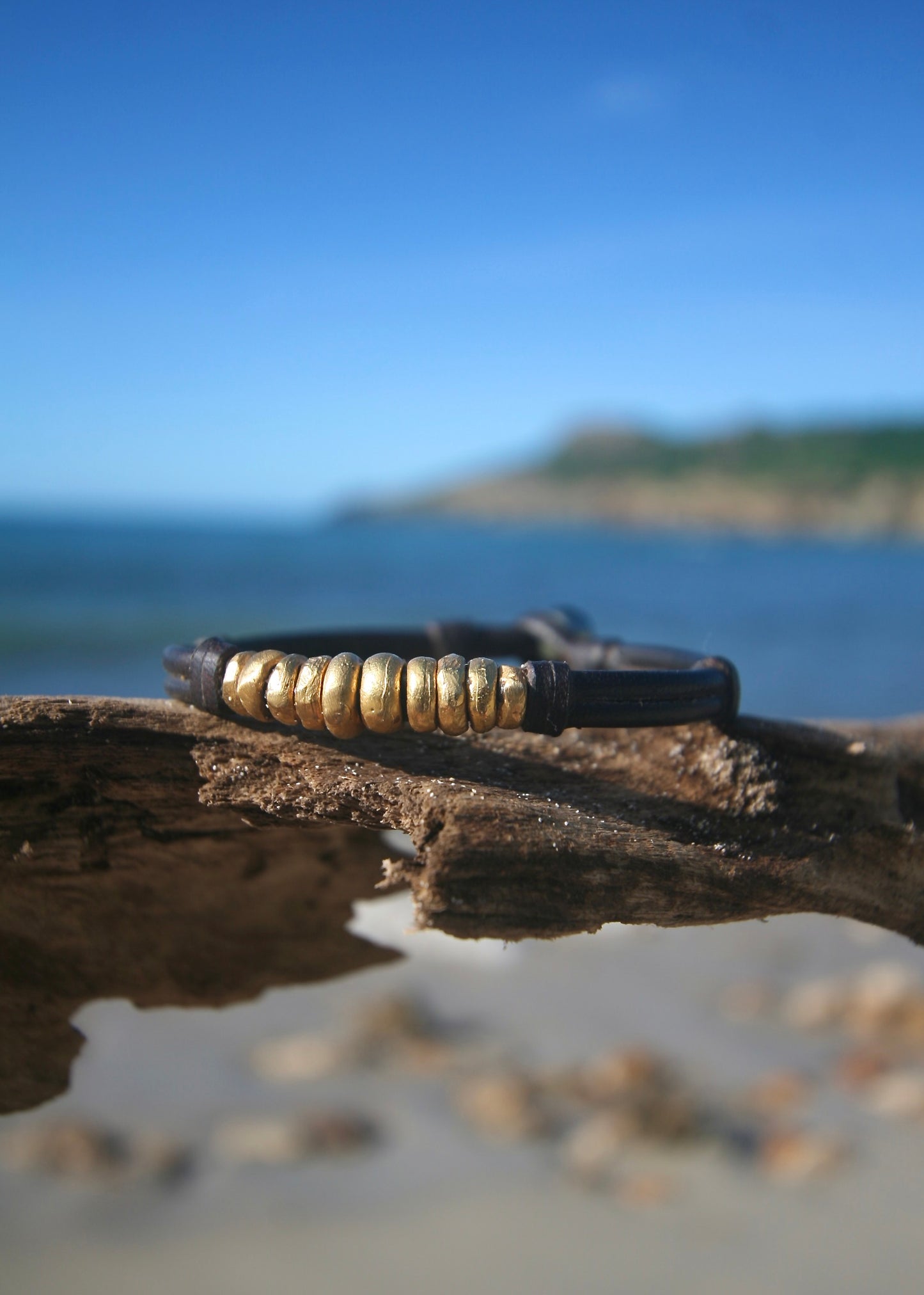 Trésors de St Barth solid gold bracelet on leather lifestyle shot with wrist extended toward the ocean