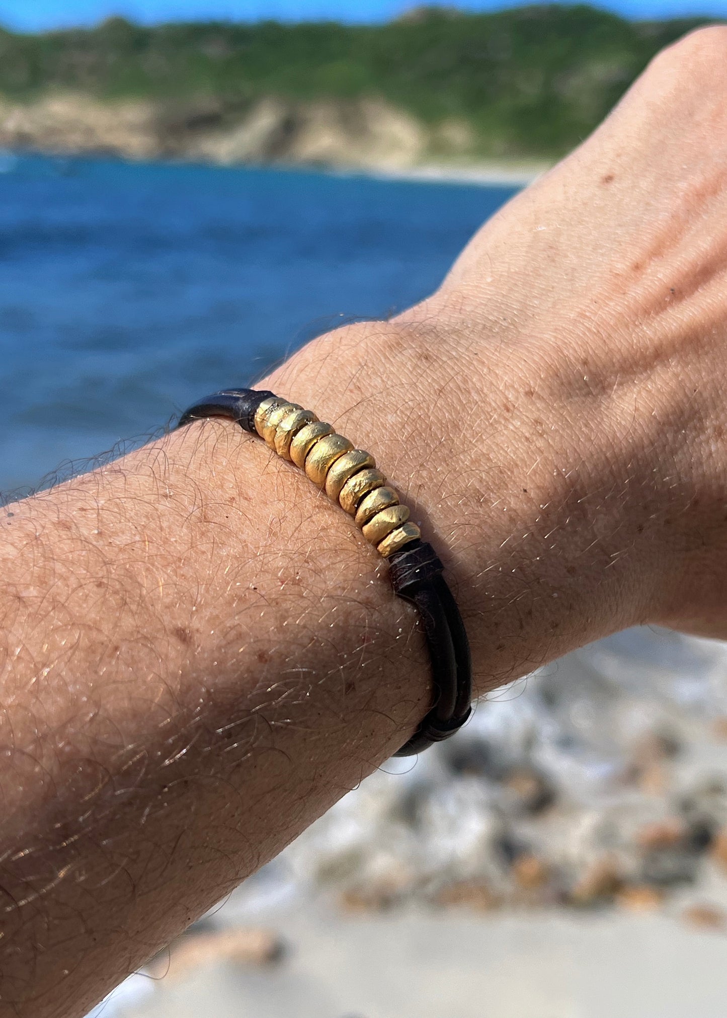 18K solid gold beads bracelet on kangaroo leather worn on a man wrist with beach background