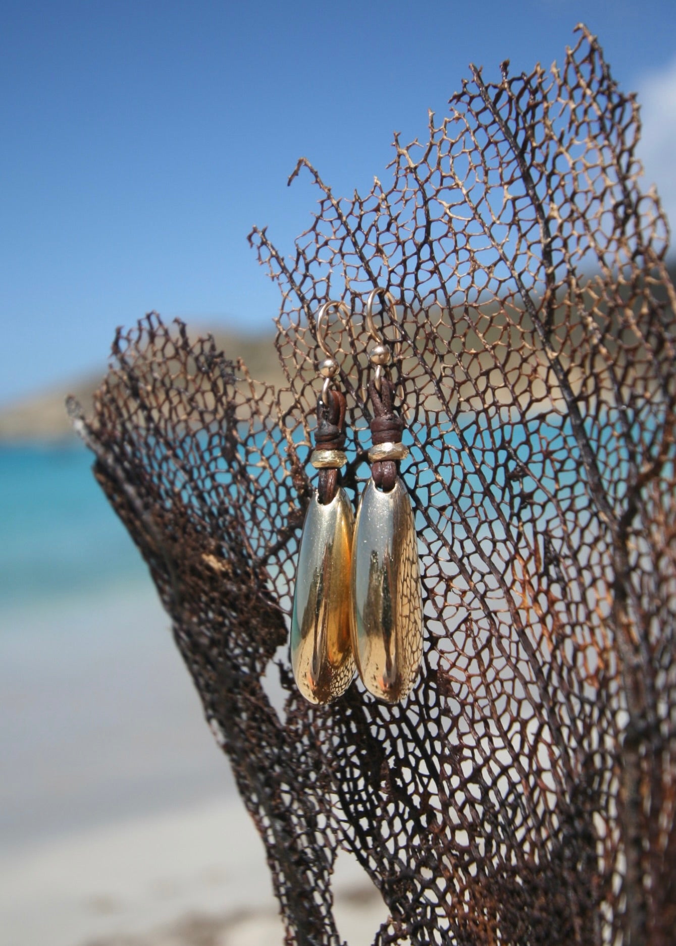 Handmade gold drop earrings hanging on driftwood, Caribbean turquoise sea