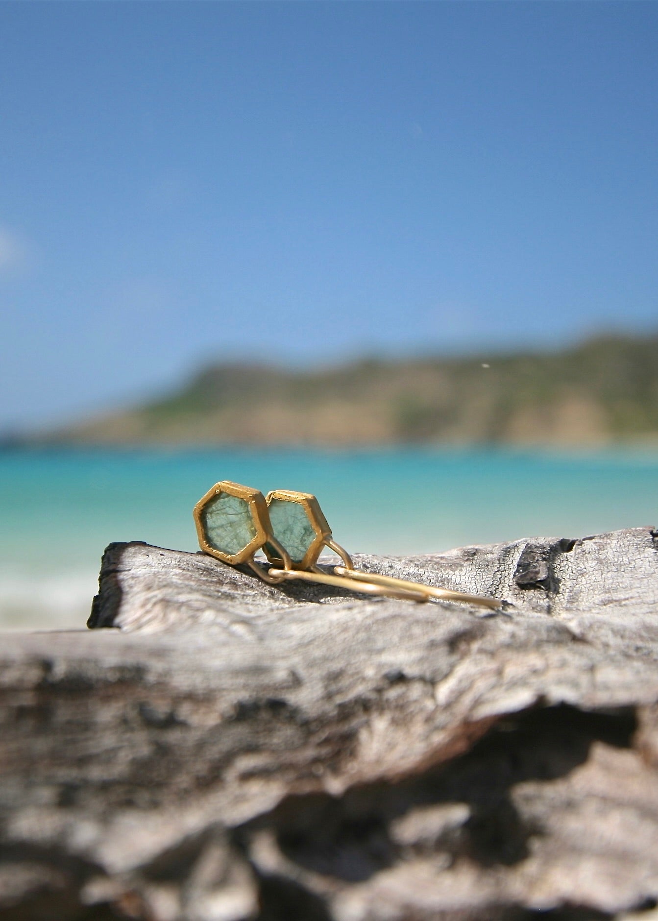 Raw emerald gold drop earrings on driftwood, St Barth island backdrop