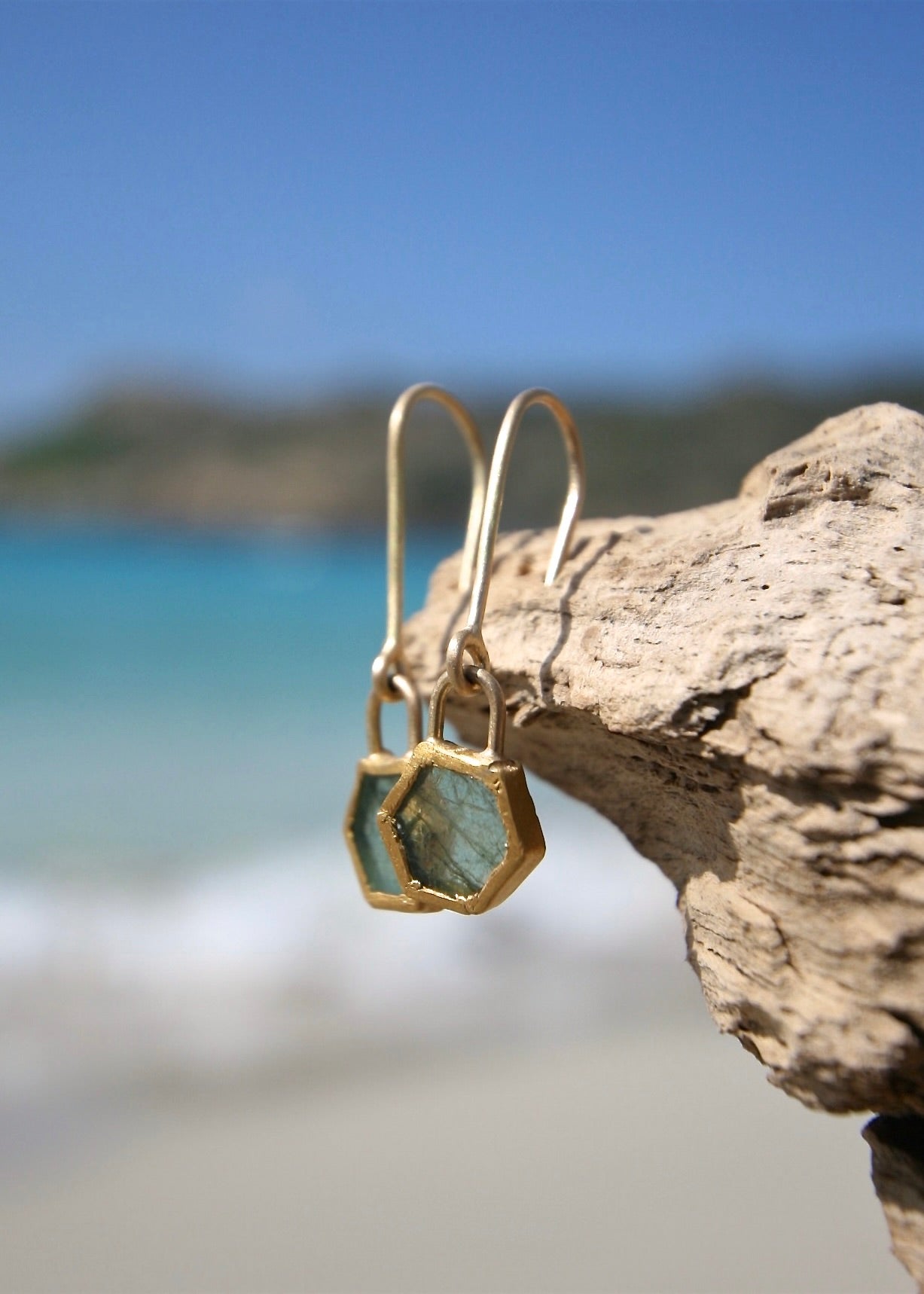 Raw emerald hexagon drop earrings on driftwood, Caribbean sea
