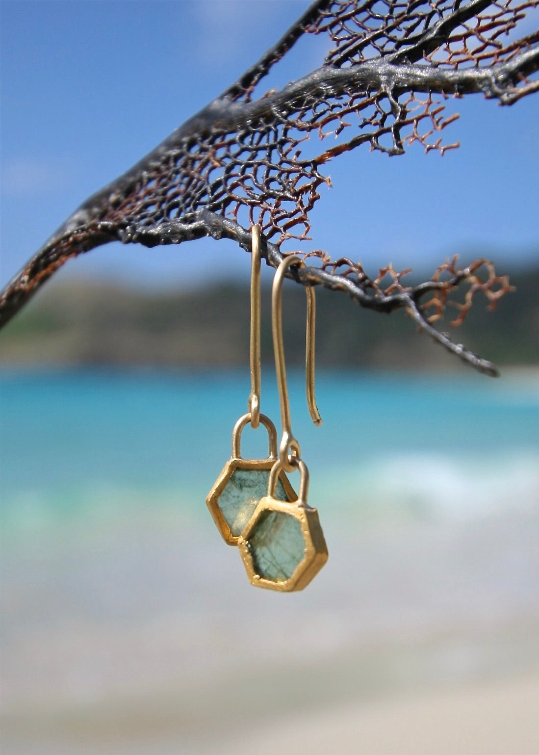 Raw emerald 24K gold hexagonal drop earrings on sea net, St Barth beach