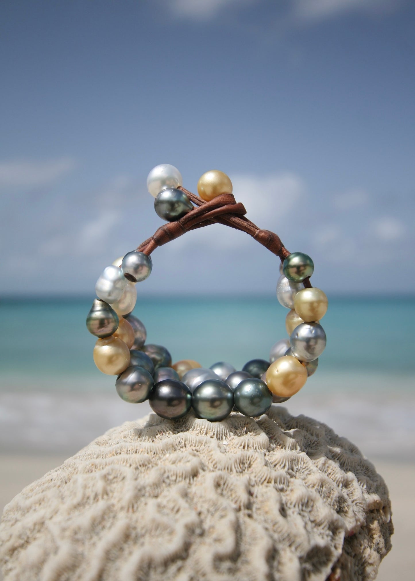 Multicolor cultured pearl cuff bracelet on sand, turquoise sea backdrop