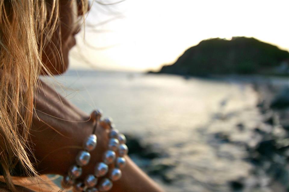 Wrist wrapped in layered Tahitian pearl bracelets, gazing at the sunset