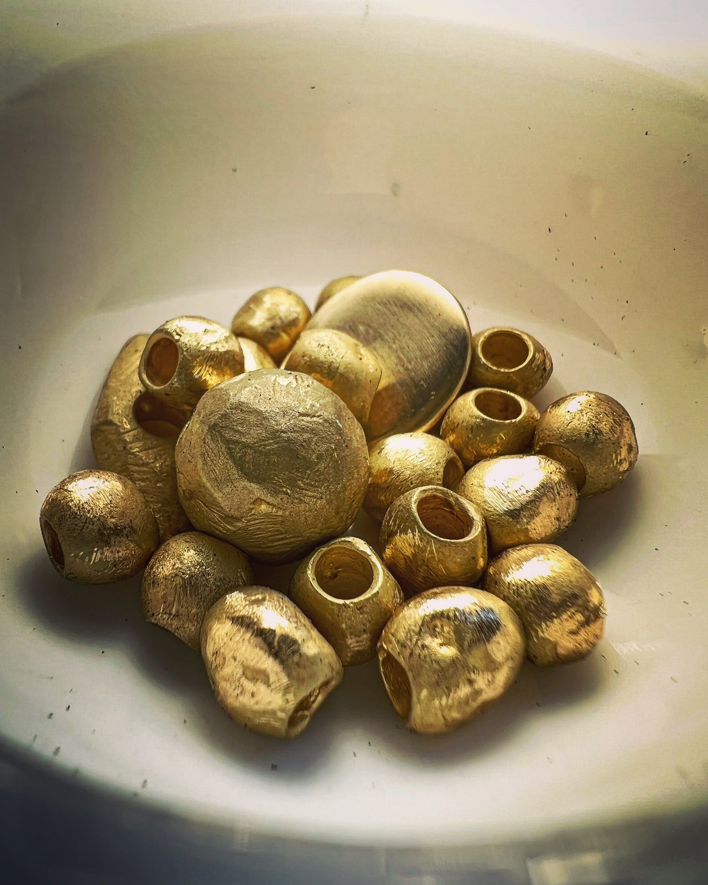 A pile of textured gold-colored seed beads with hollow centers, resting inside a white ceramic bowl.