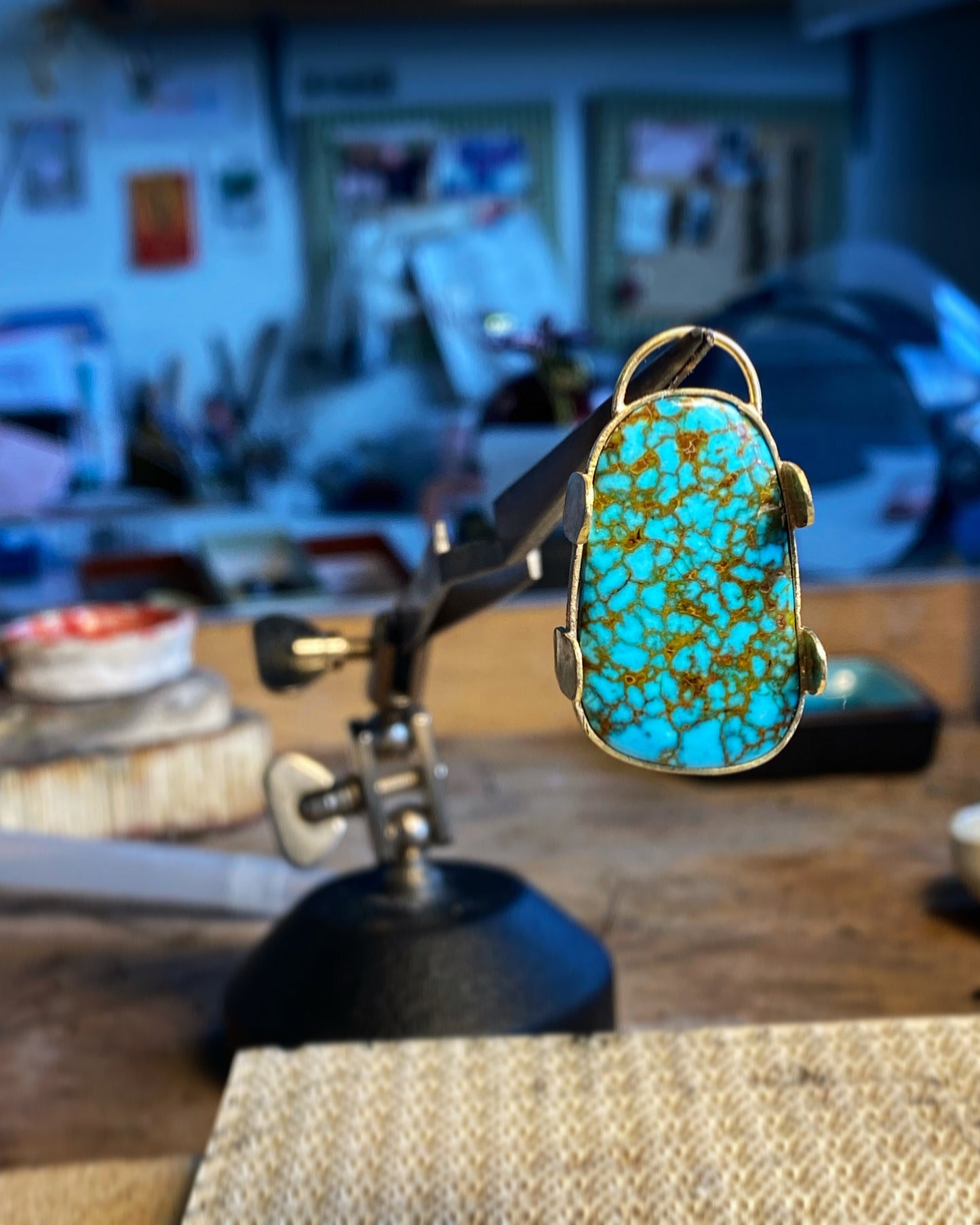 Nevada turquoise stone set in gold prongs, held in workshop jeweler's clamp