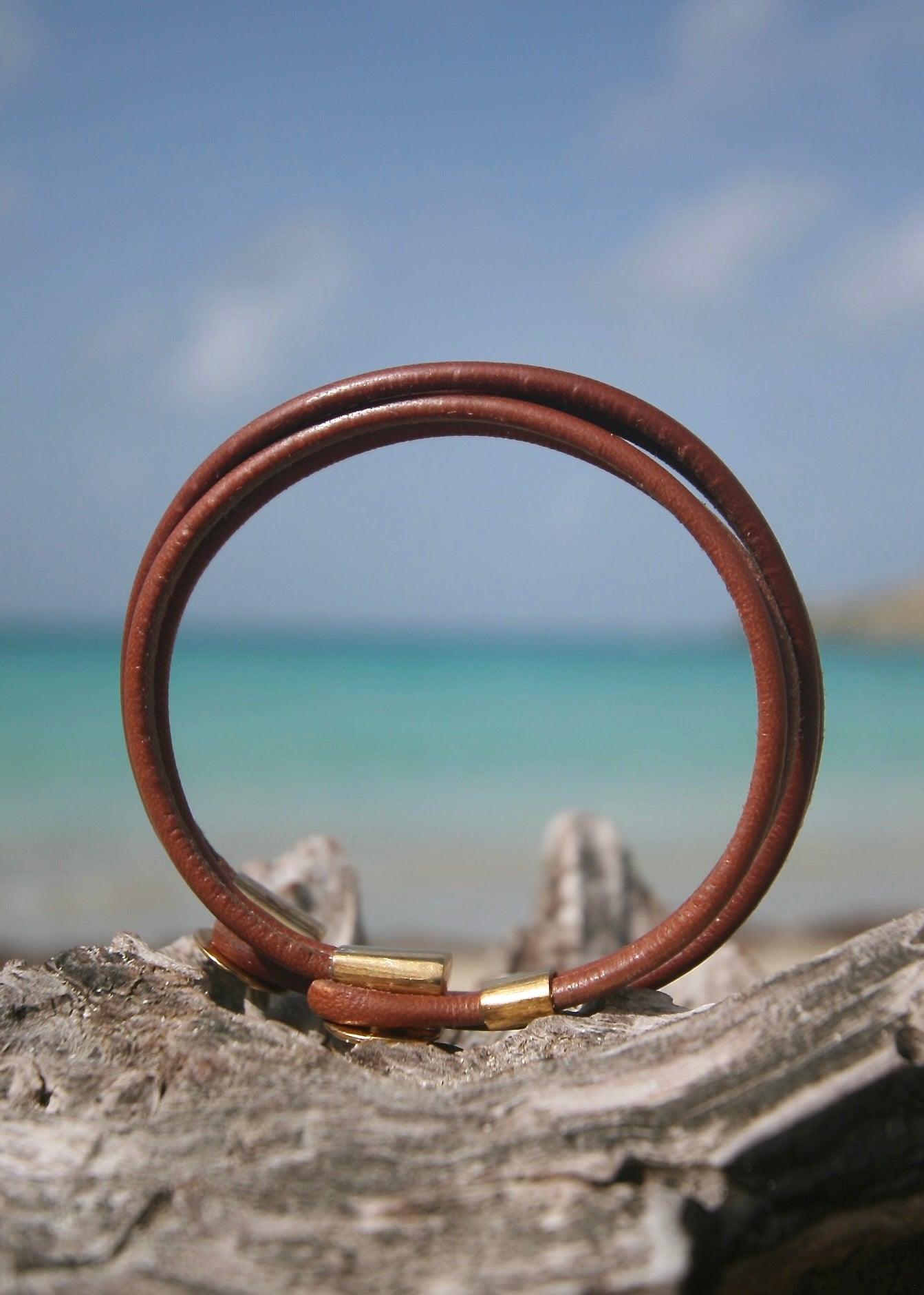 18K gold Greek coin leather bracelet on driftwood, Caribbean sea