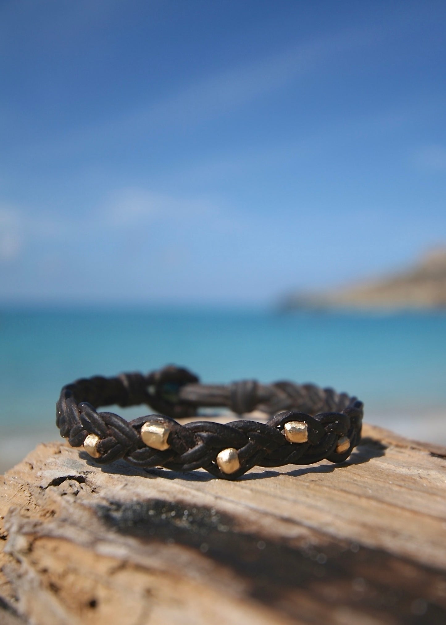 Handmade braided leather gold bead bracelet on driftwood, Caribbean turquoise sea