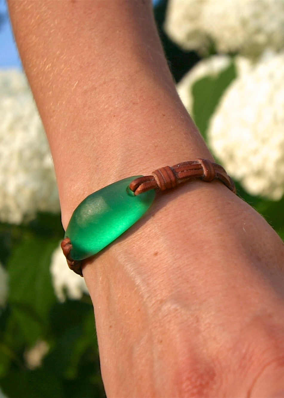 Crystal glass bracelet worn on wrist showing luminous green sculpted glass bead on knotted leather