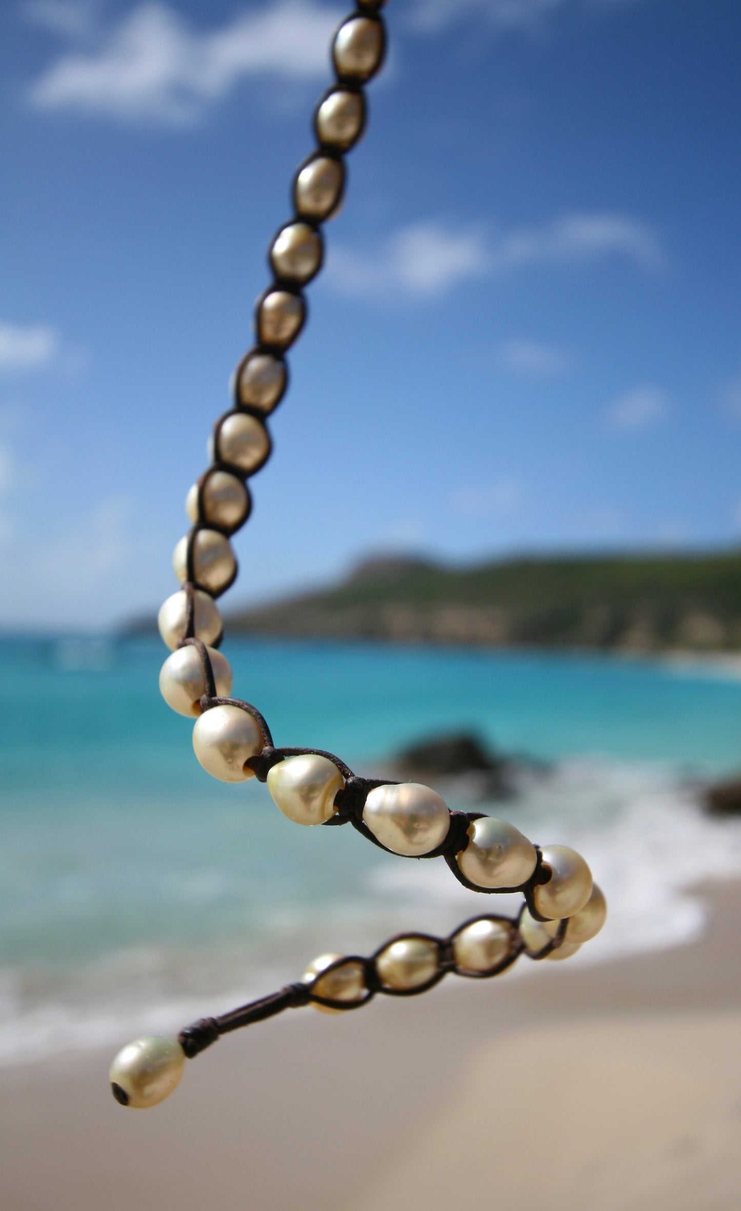 Long pearl and leather double wrap bracelet draped against the turquoise bay