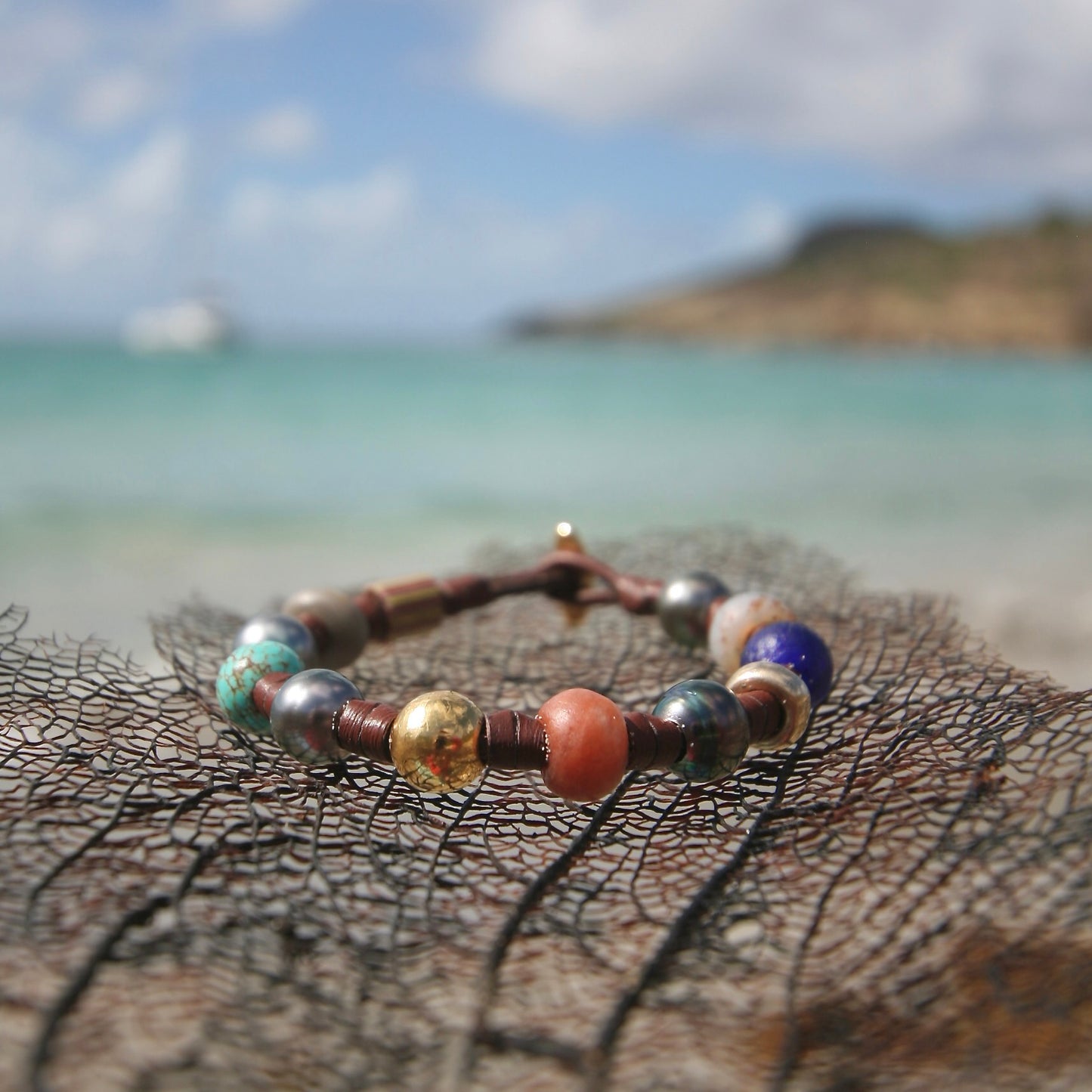 Bracelet resting on dried sea fan, St. Barth hillside and turquoise sea
Treasure bracelet with Tahitian pearls, 18k solid gold, turquoise, lapis lazuli, carnelian and rare beads on kangaroo leather, on sea fan with St. Barth sea — treasures leather bracelet from St. Barth.