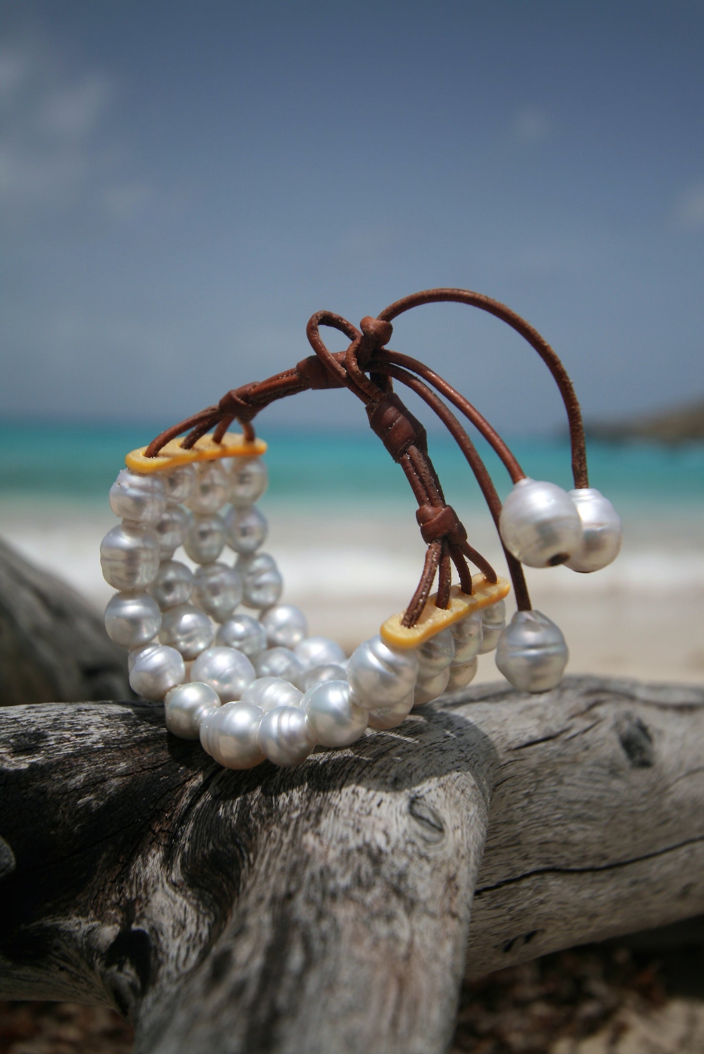 white pearl bracelets cuff with leather ties, laid on driftwood and mother of pearl