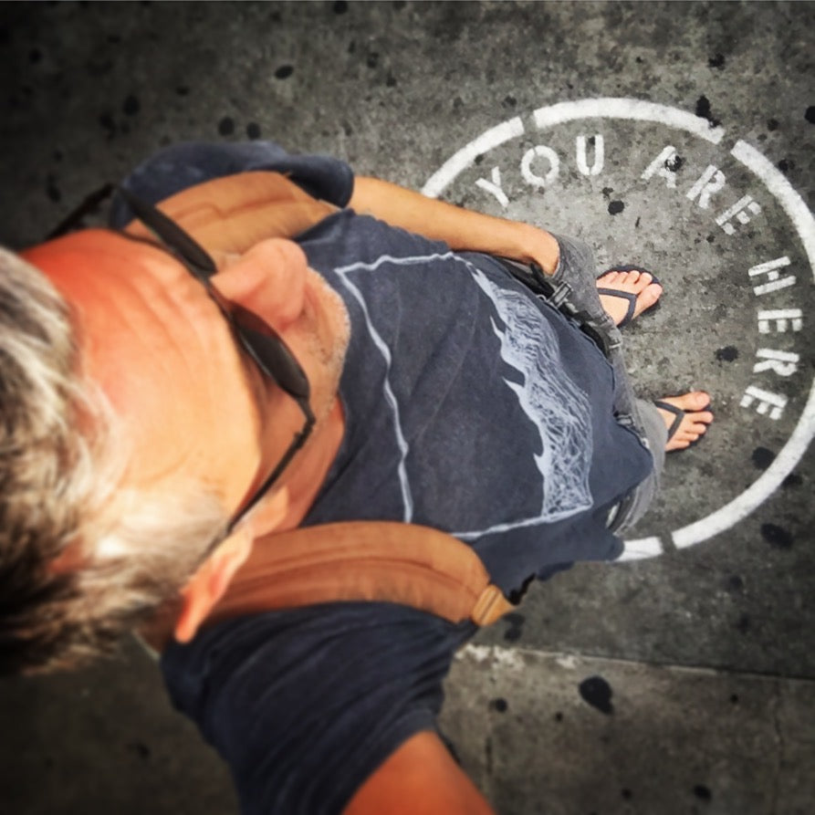 Ted Deltour lying on the ground at a "You Are Here" street marker