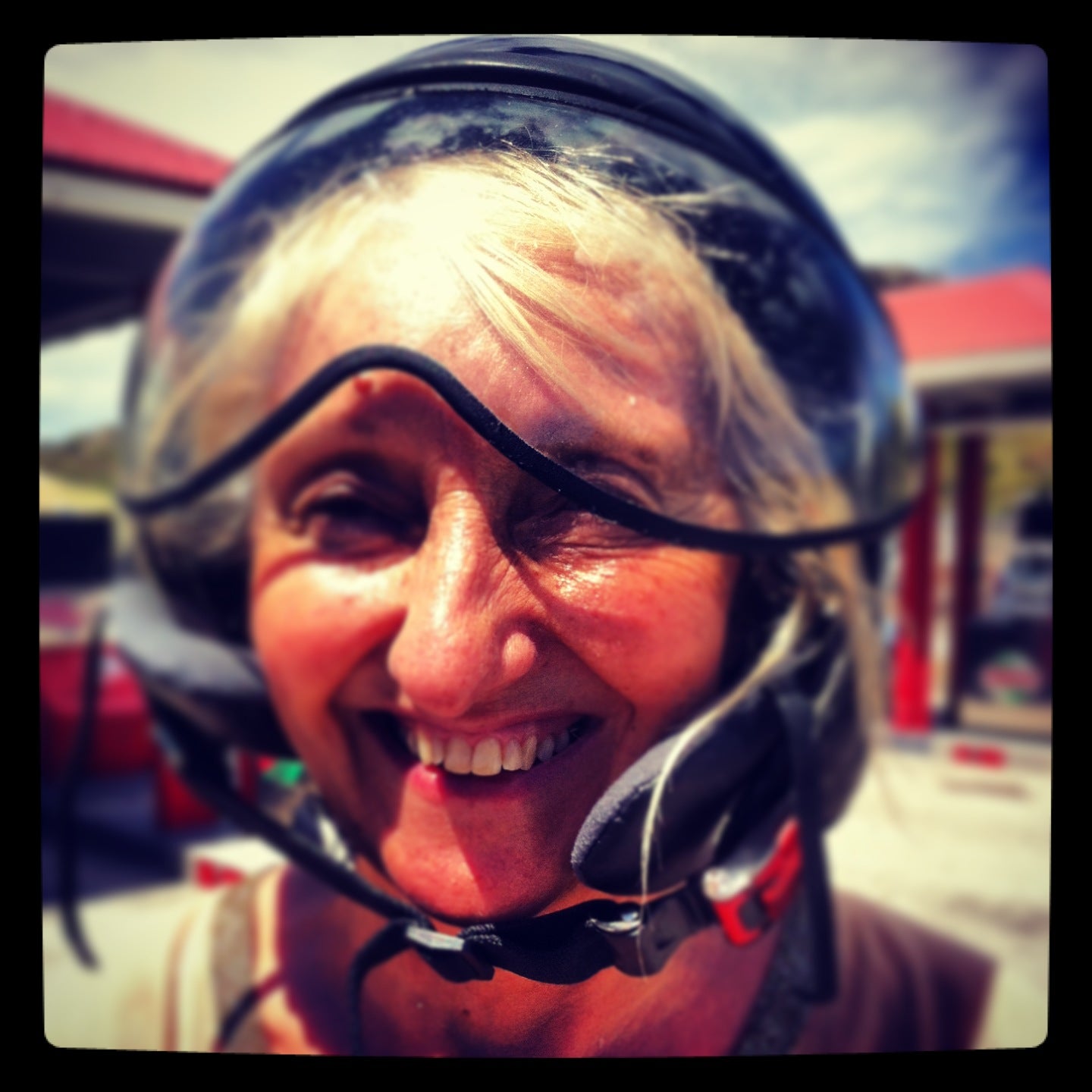 Smiling woman wearing a motorcycle helmet, sunny St Barth street scene