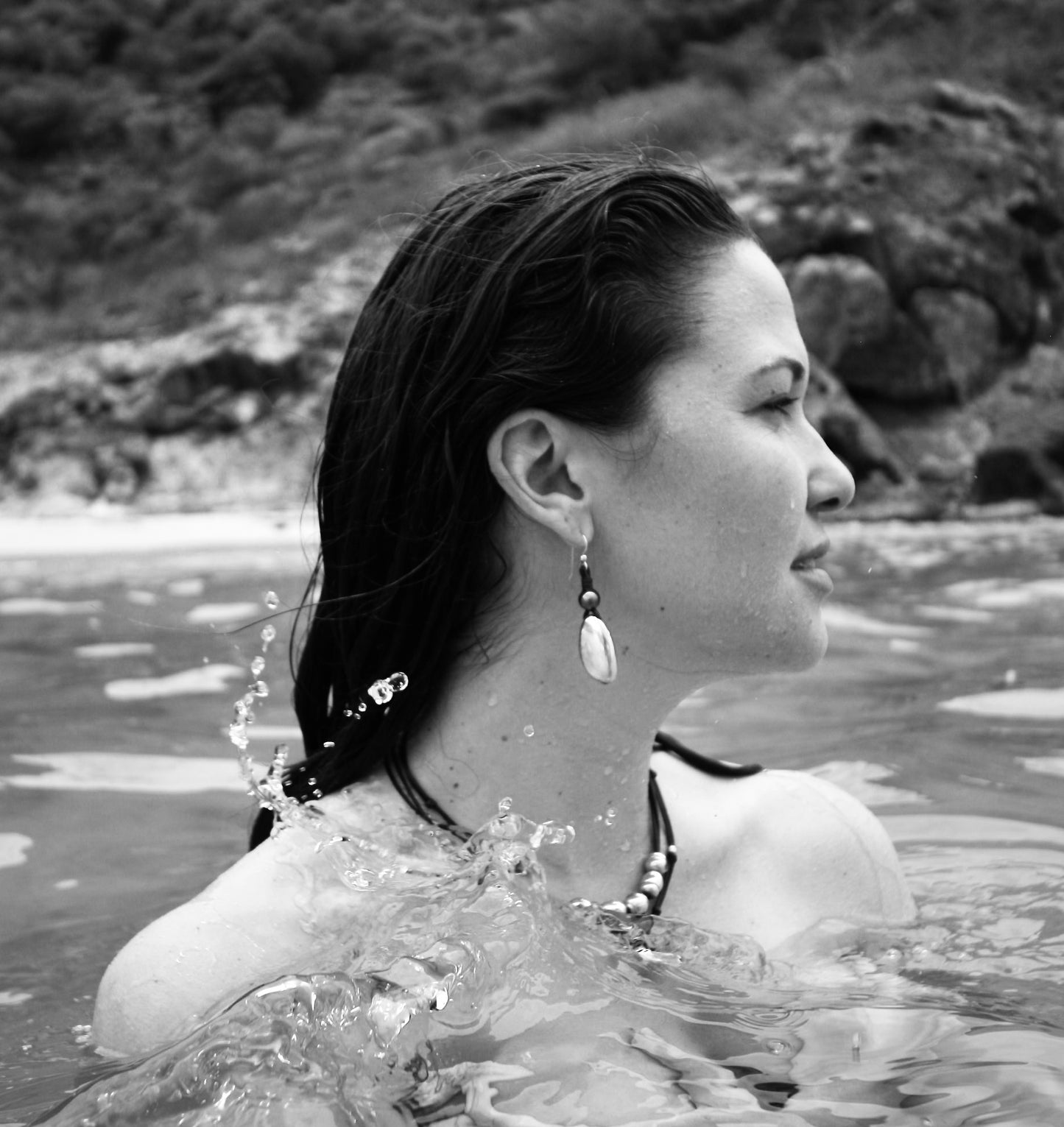 Woman in the ocean wearing pearl and gold drop earrings, black and white