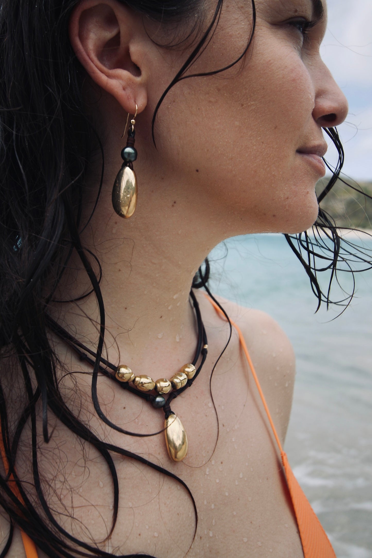 Woman wearing gold beaded leather necklace and pearl earring, beach day