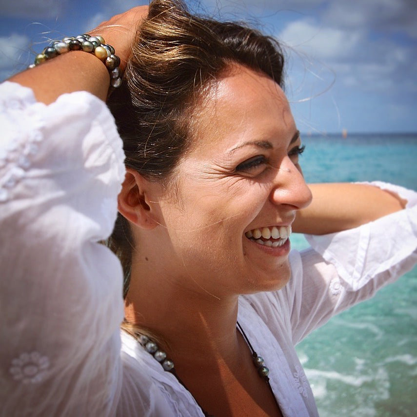 Laughing woman wearing layered Tahitian pearl bracelets, wind in her hair