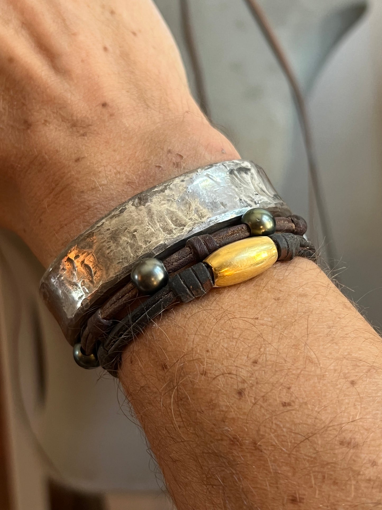 Wrist wearing a hammered silver cuff with leather, pearls  and gold bead accent
