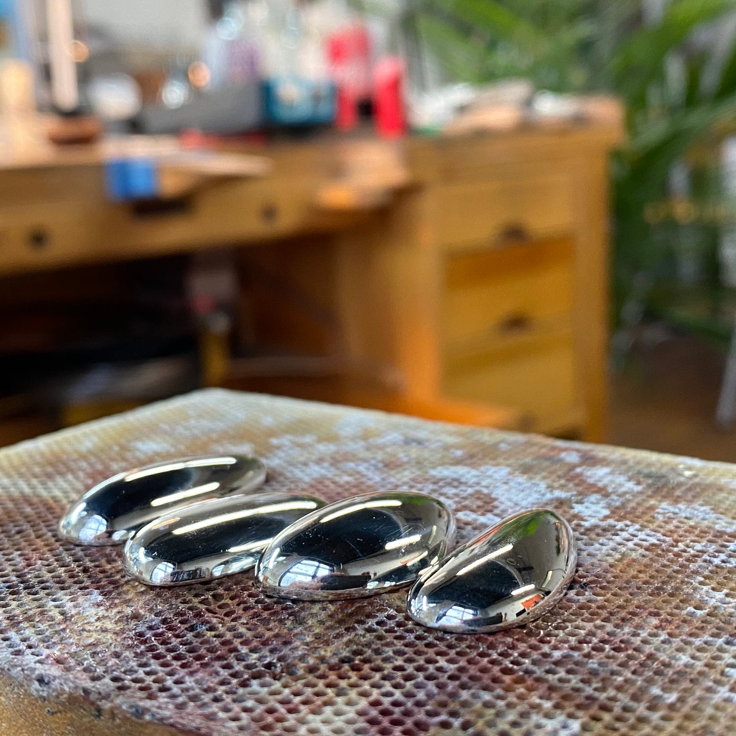 Hand-sculpted silver pebble pendants before finishing, jewelry workshop bench