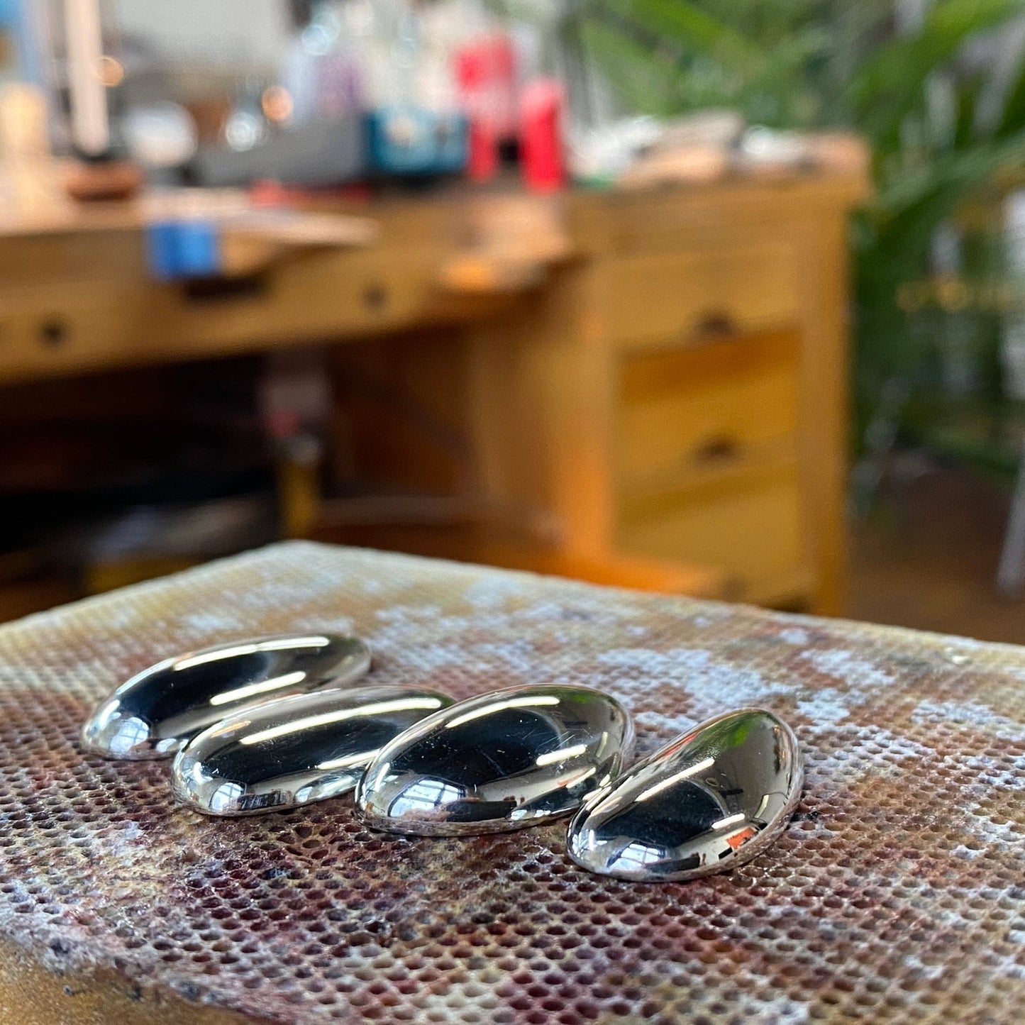Hand-sculpted silver pebble pendants before finishing, jewelry workshop bench