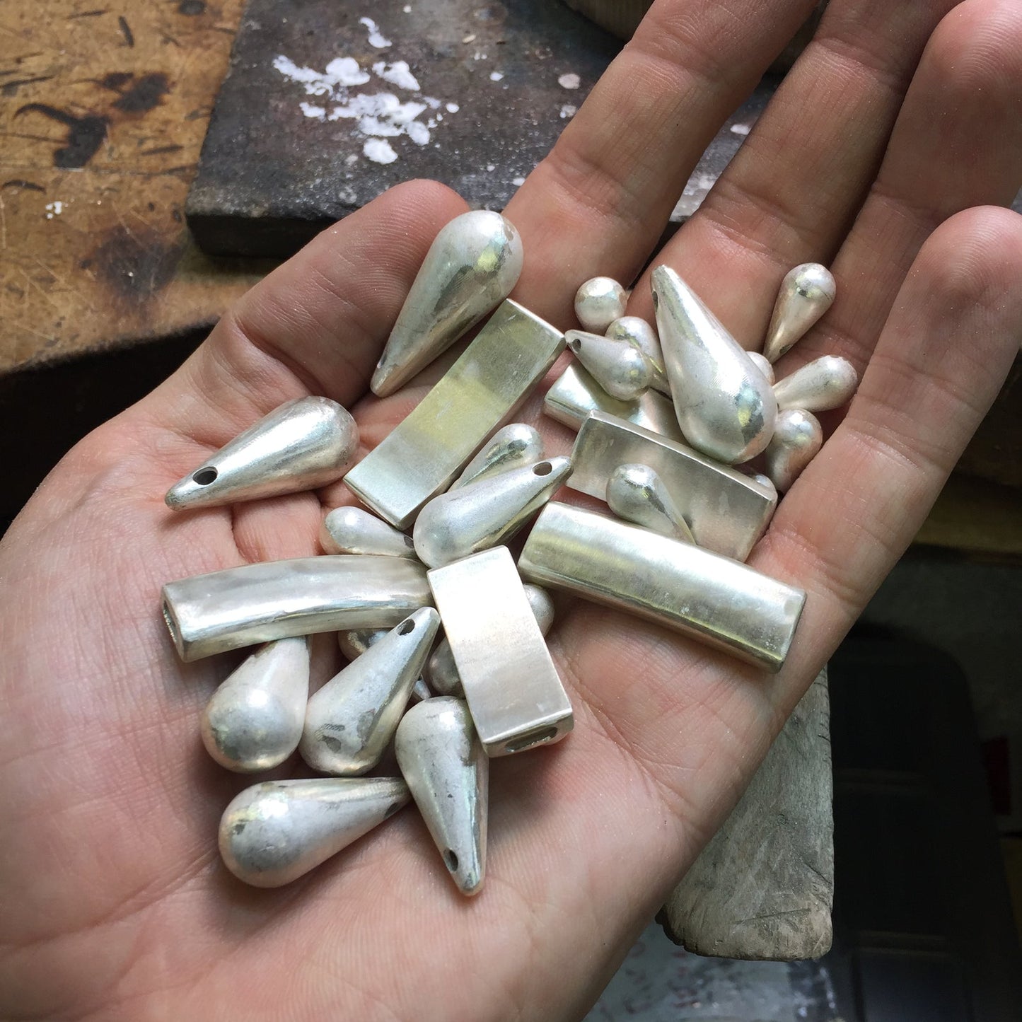Handmade silver drop and bar pendants held in hand, jewelry workshop