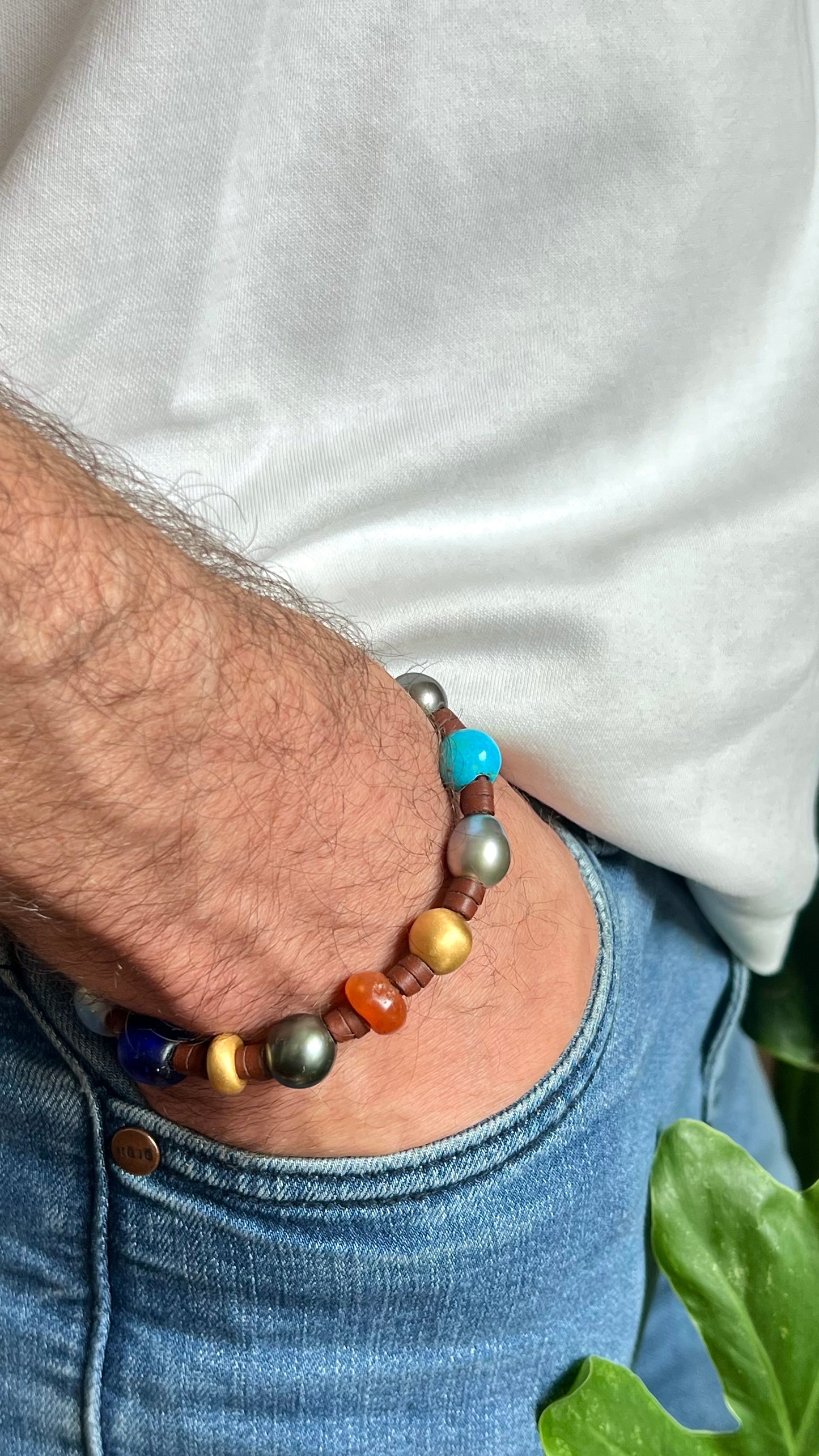 Lifestyle wrist shot on man's wrist, white t-shirt and denim, casual urban setting
Treasure bracelet with Tahitian pearls, 18k gold and rare multicolor beads on kangaroo leather worn casually with jeans — unisex handmade bracelet by Trésors de St Barth.