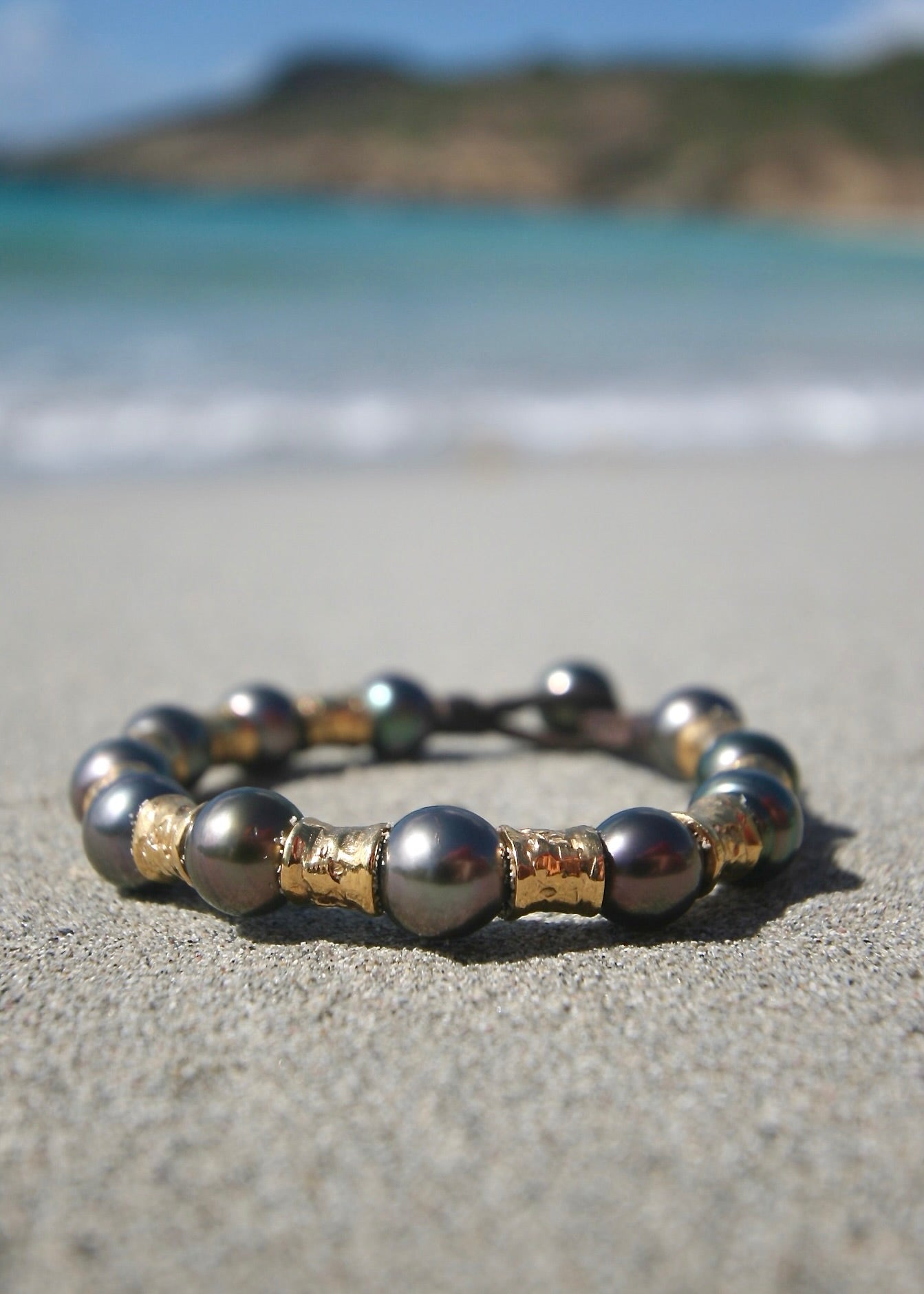 Tahitian black pearl and 18k gold bead leather bracelet standing in St. Barth beach sand — leather bracelet knotted with pearls and gold from St. Barth.