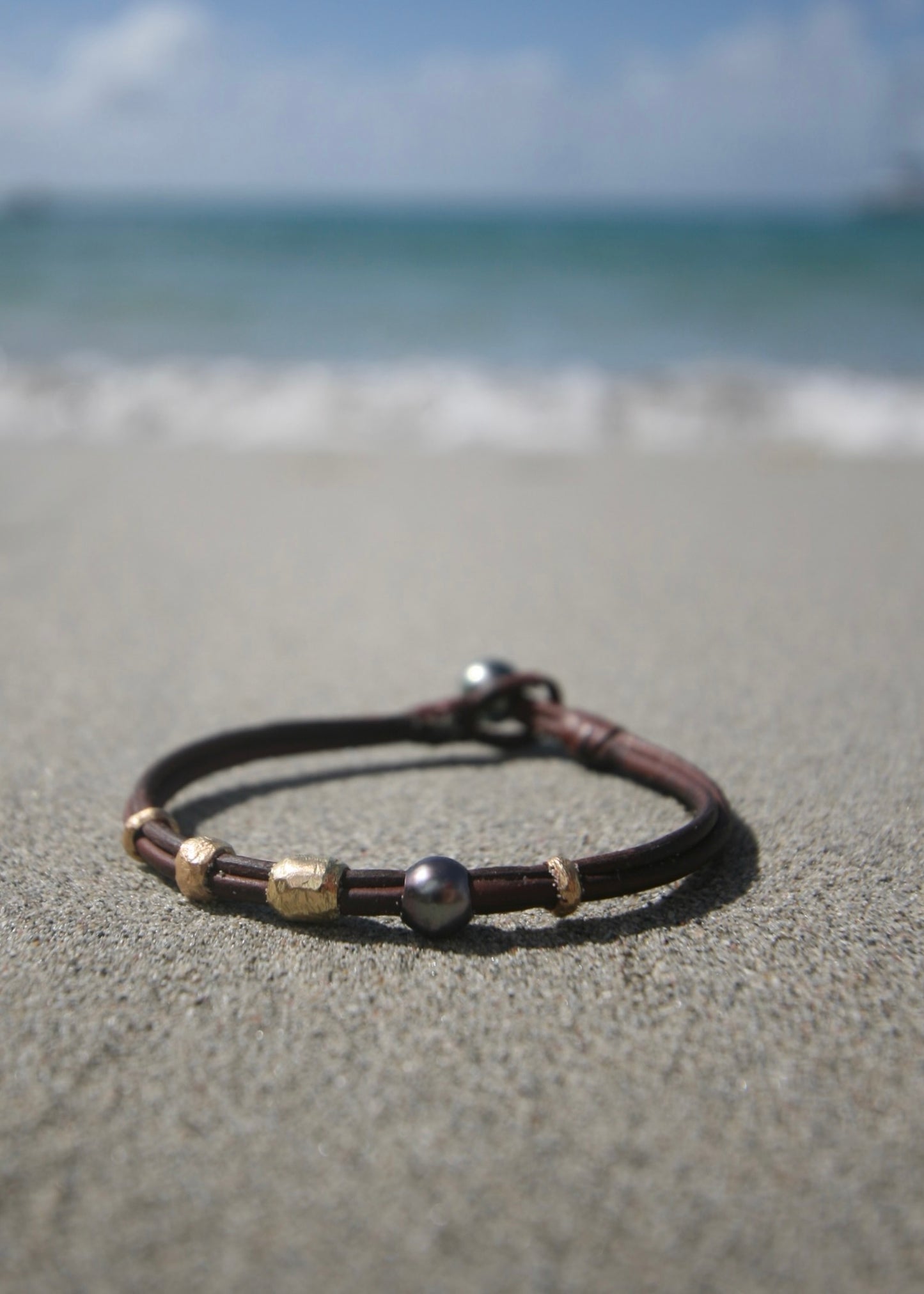 Minimalist gold pearl leather bracelet on sand, Caribbean turquoise sea