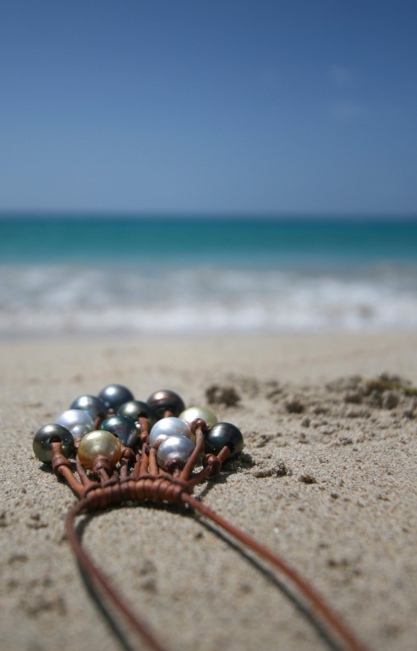 Tahitian golden pearl cascade necklace detail on sand, blue sky backdrop