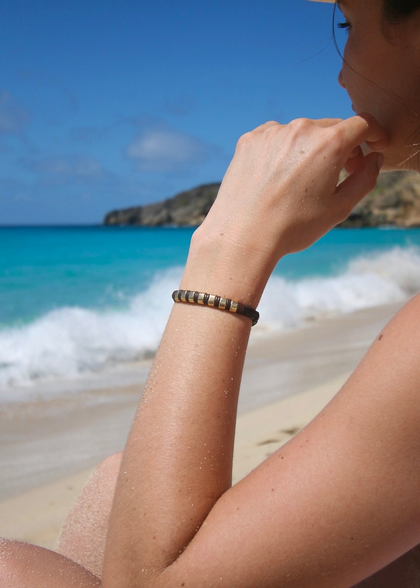 Solid gold ingot leather bracelet worn on wrist, Caribbean turquoise sea