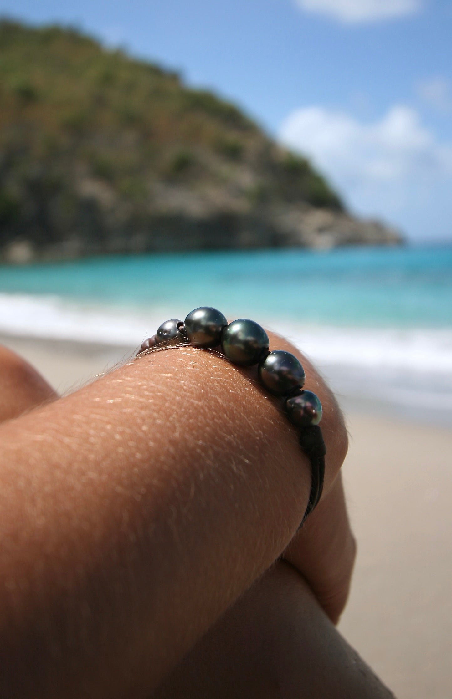 Tahitian black pearl gradient bracelet on leather worn on wrist, St Barth beach