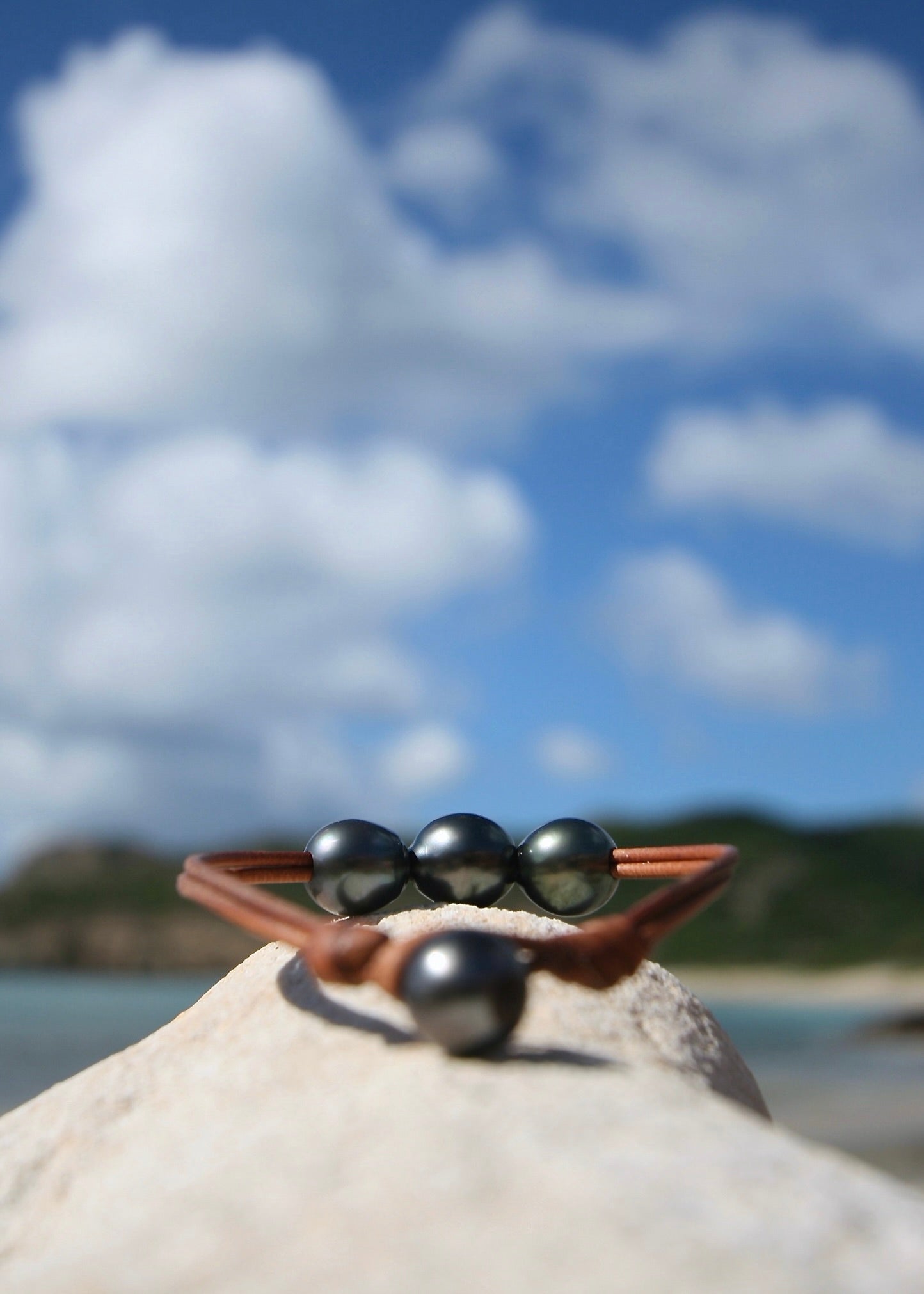 Three dark Tahitian pearl leather bracelet on rock, Caribbean blue sky