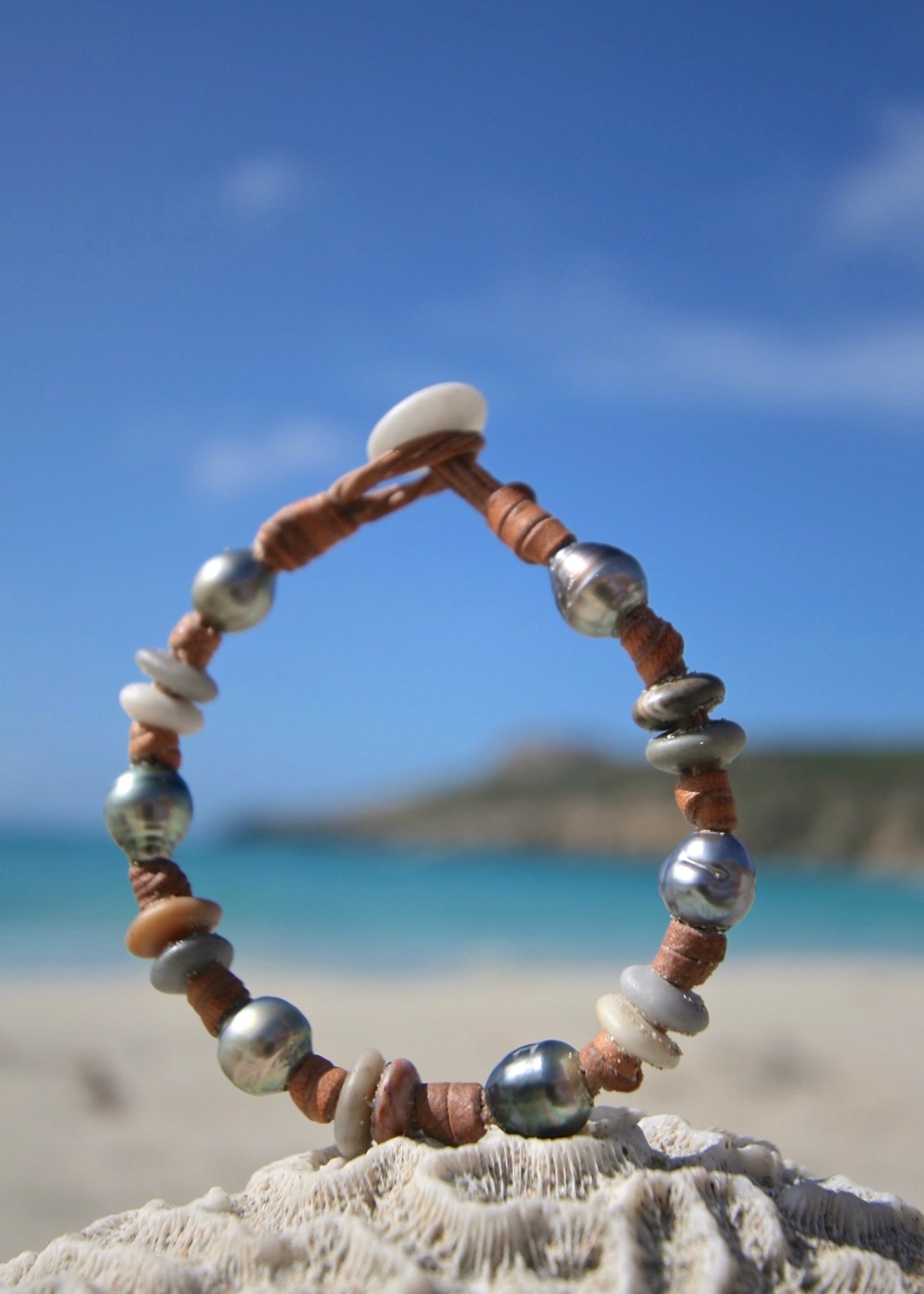 Handmade Tahitian pearl sea pebble leather bracelet on sand, Caribbean sea