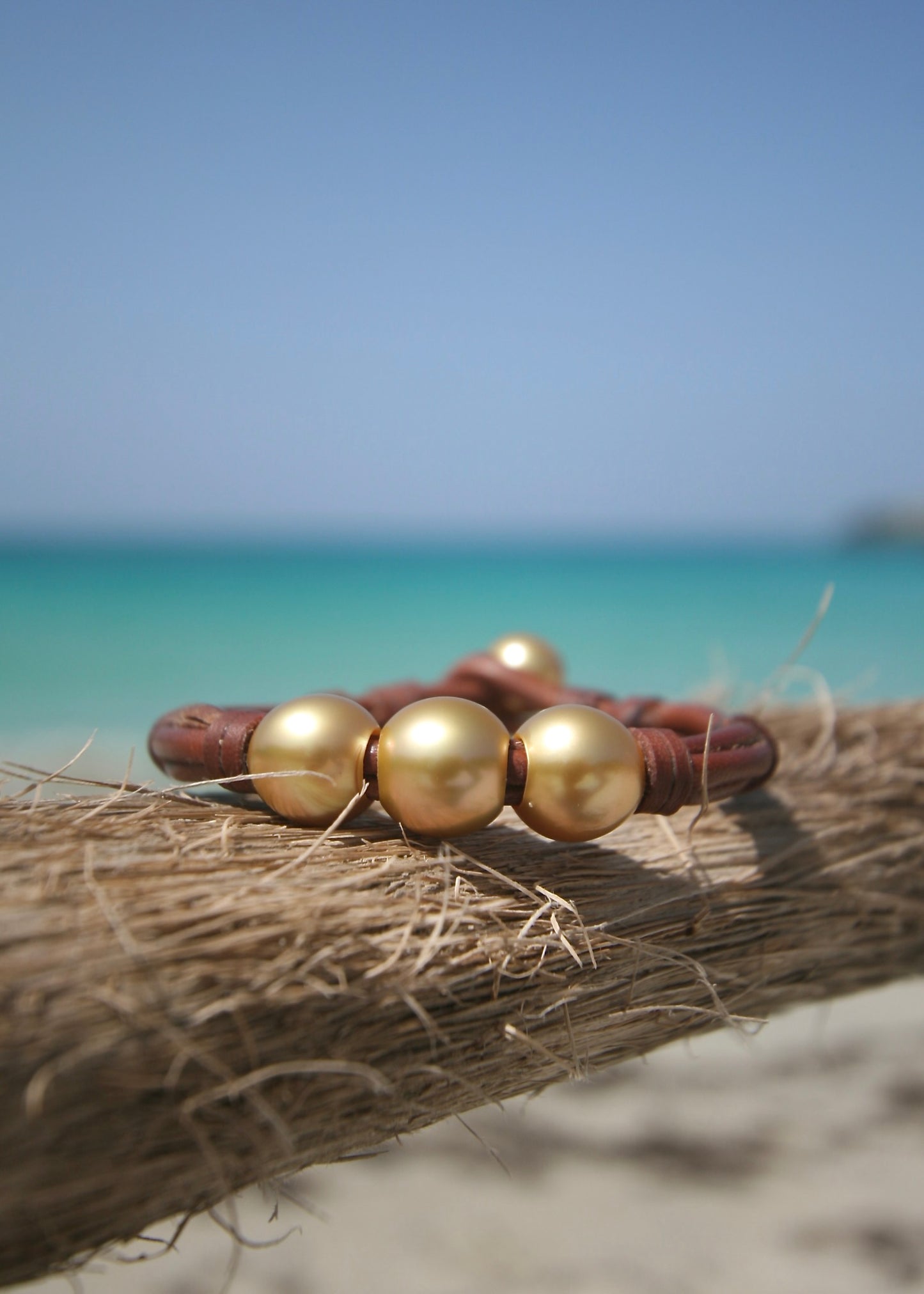 Close-up of three AA grade Australian golden pearls on hand-knotted kangaroo leather against driftwood