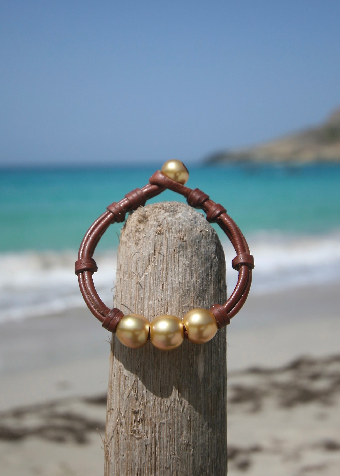 Handmade golden pearl bracelet full view showing pearl clasp and kangaroo leather knots on wooden post