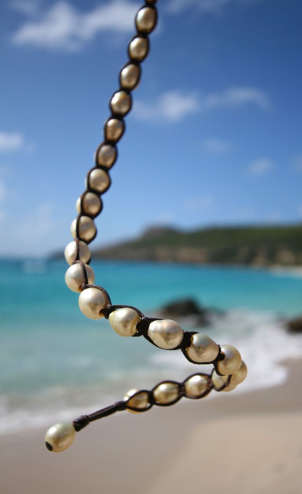 Cream gold pearl beaded necklace on cord with beach in background, one of a kind jewelry St Barth