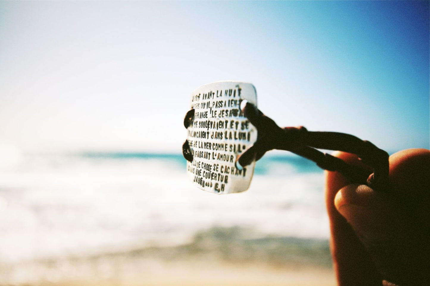Engraved silver poem pendant held up against beach backdrop, one of a kind jewelry St Barth