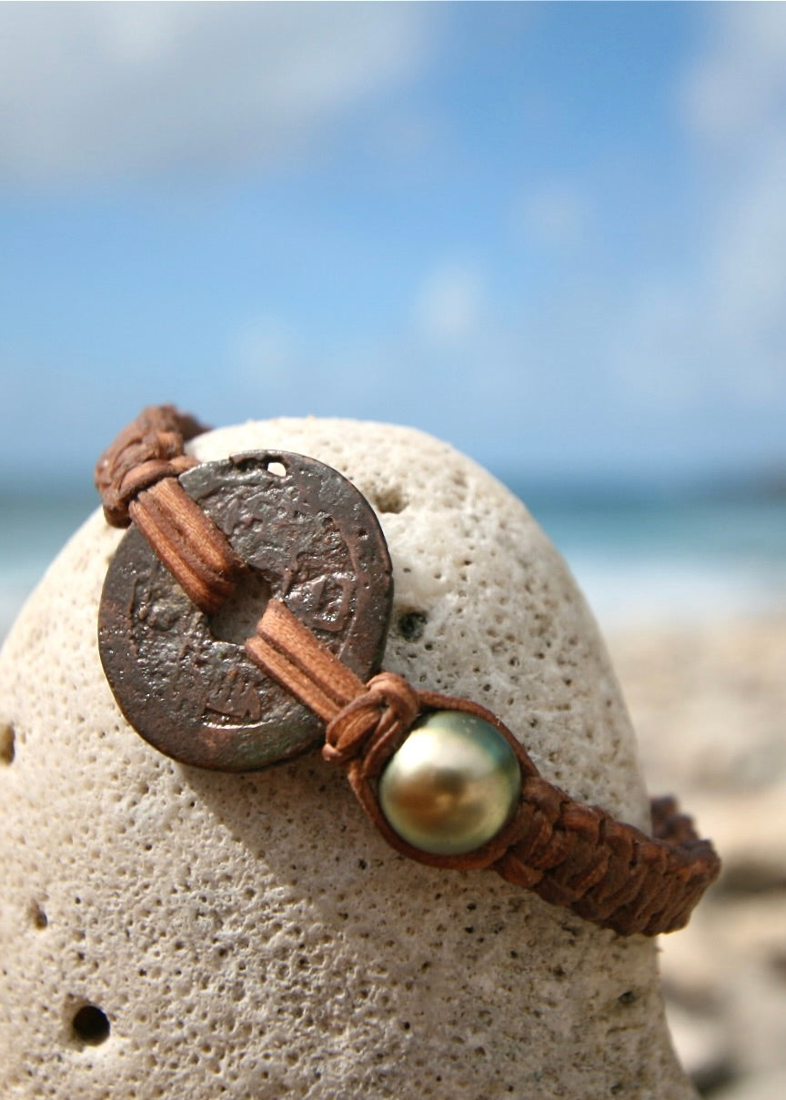 Close up of genuine Tokugawa period Japanese copper coin and dark Tahitian pearl on braided leather