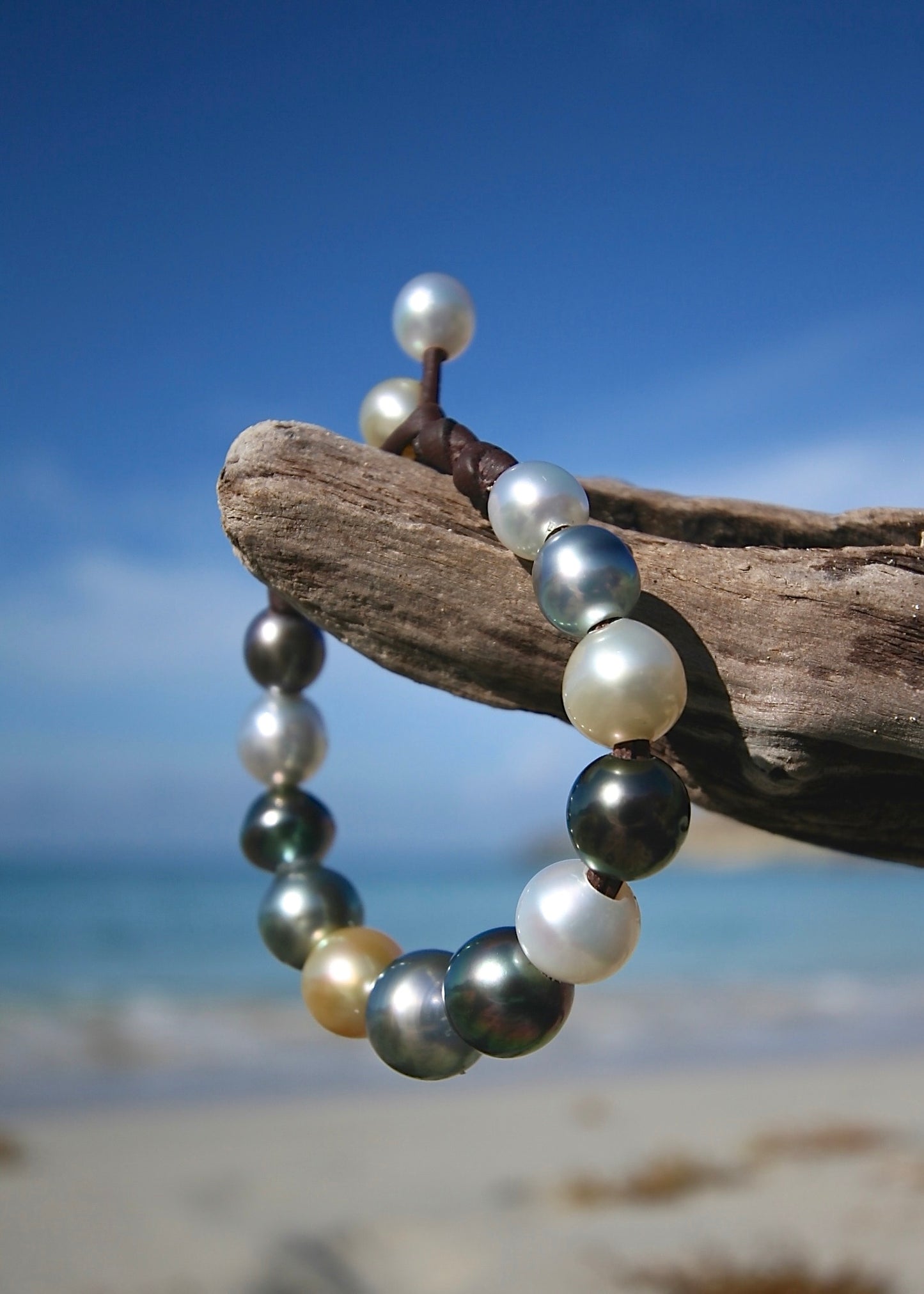 Gradient pearl bracelet featuring silver gold and dark Tahitian pearls on leather with Caribbean beach