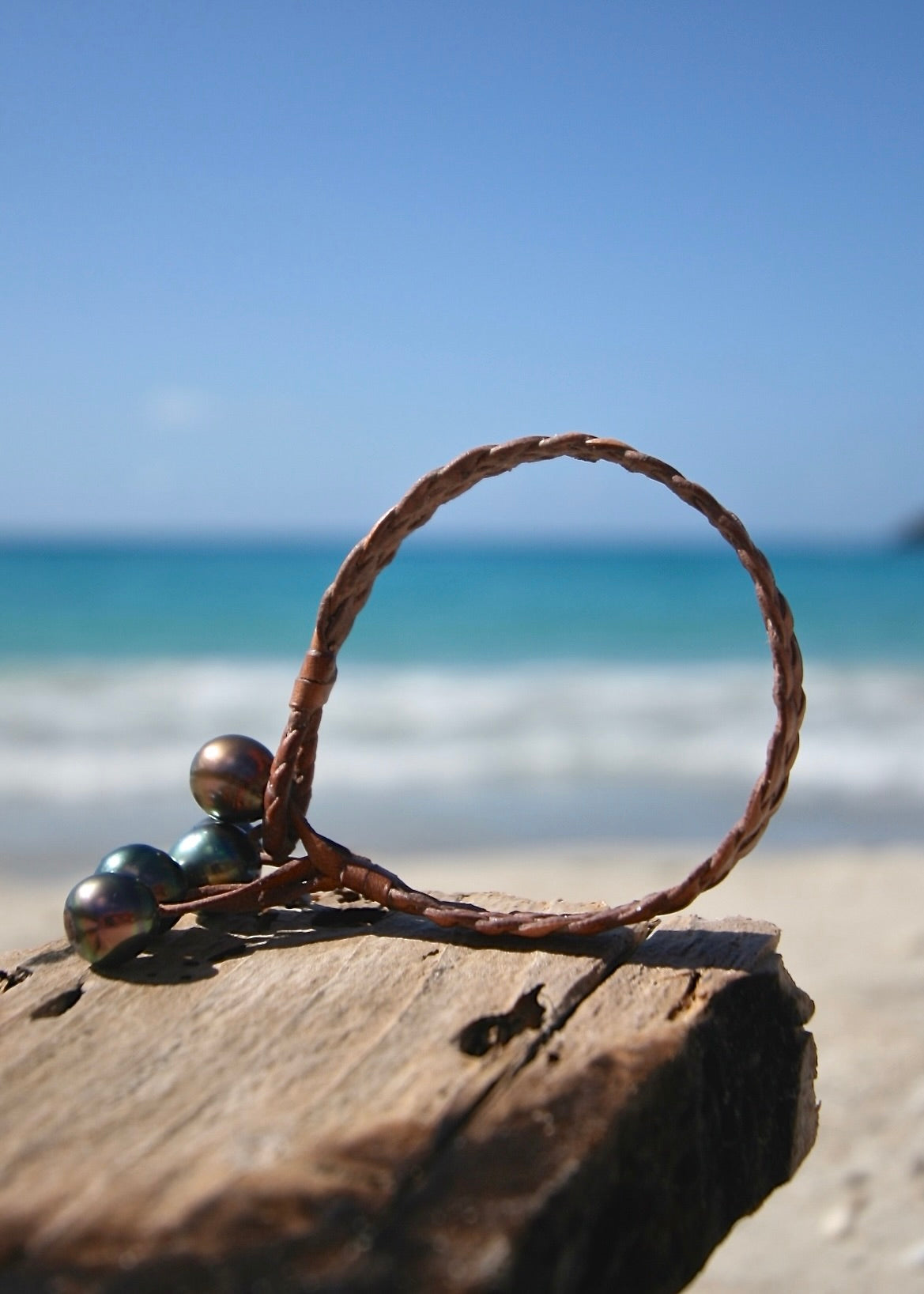 Tahitian pearl braided bracelet standing on driftwood showing five dark pearl tassel hanging freely