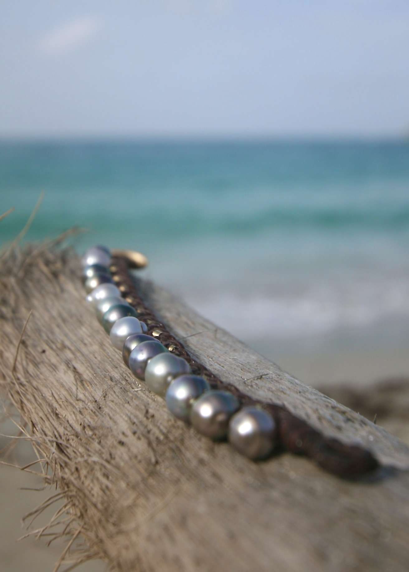 Silver Tahitian pearls aligned along hand braided kangaroo leather bracelet with 18K gold on driftwood