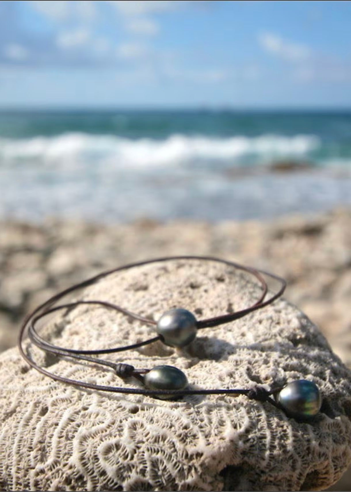 Trésors de St Barth adjustable pearl lariat laid on sand showing focal pearl and two drop pearls on leather